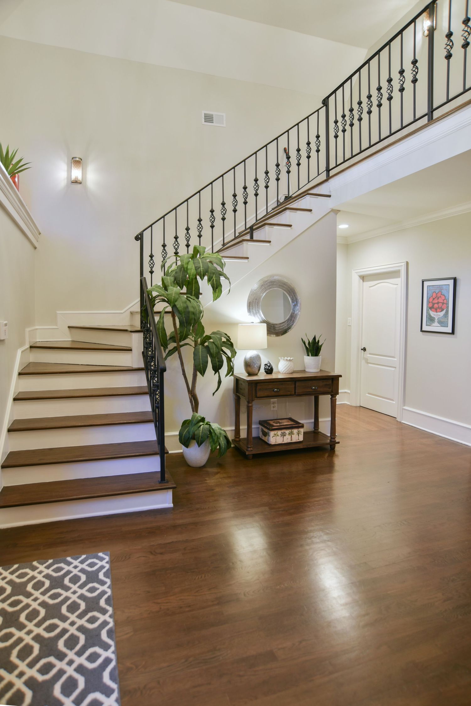 Elegant entryway features a curved wooden staircase with wrought iron railings, hardwood floors, and decorative plants.