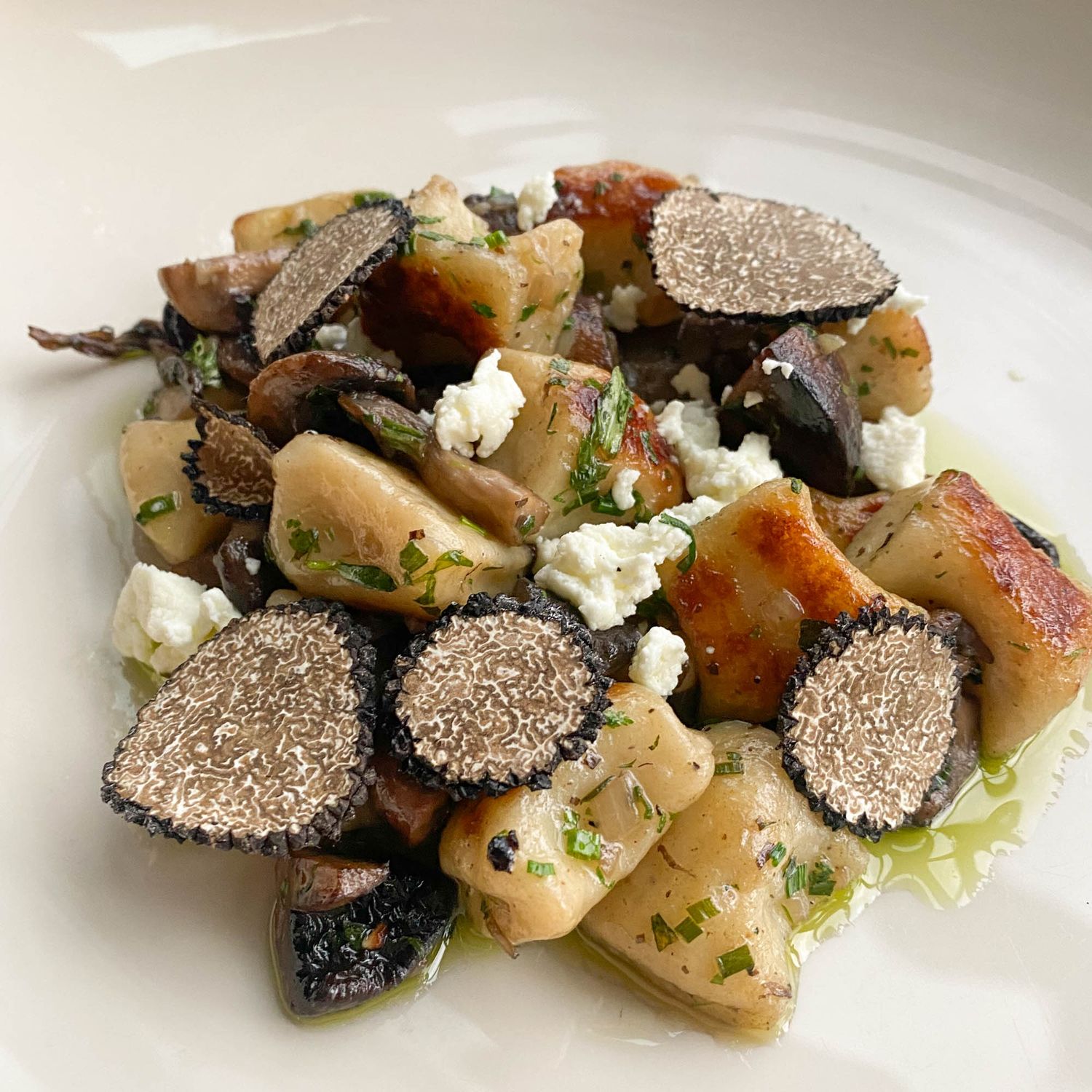 Gourmet dish featuring roasted potatoes, black truffles, and crumbled feta cheese garnished with fresh herbs on a white plate.