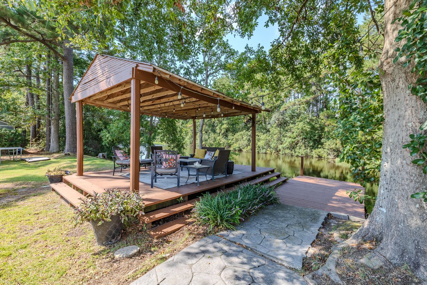 Panoramic view of a modern outdoor living space with wooden pergola and seating area surrounded by lush trees.