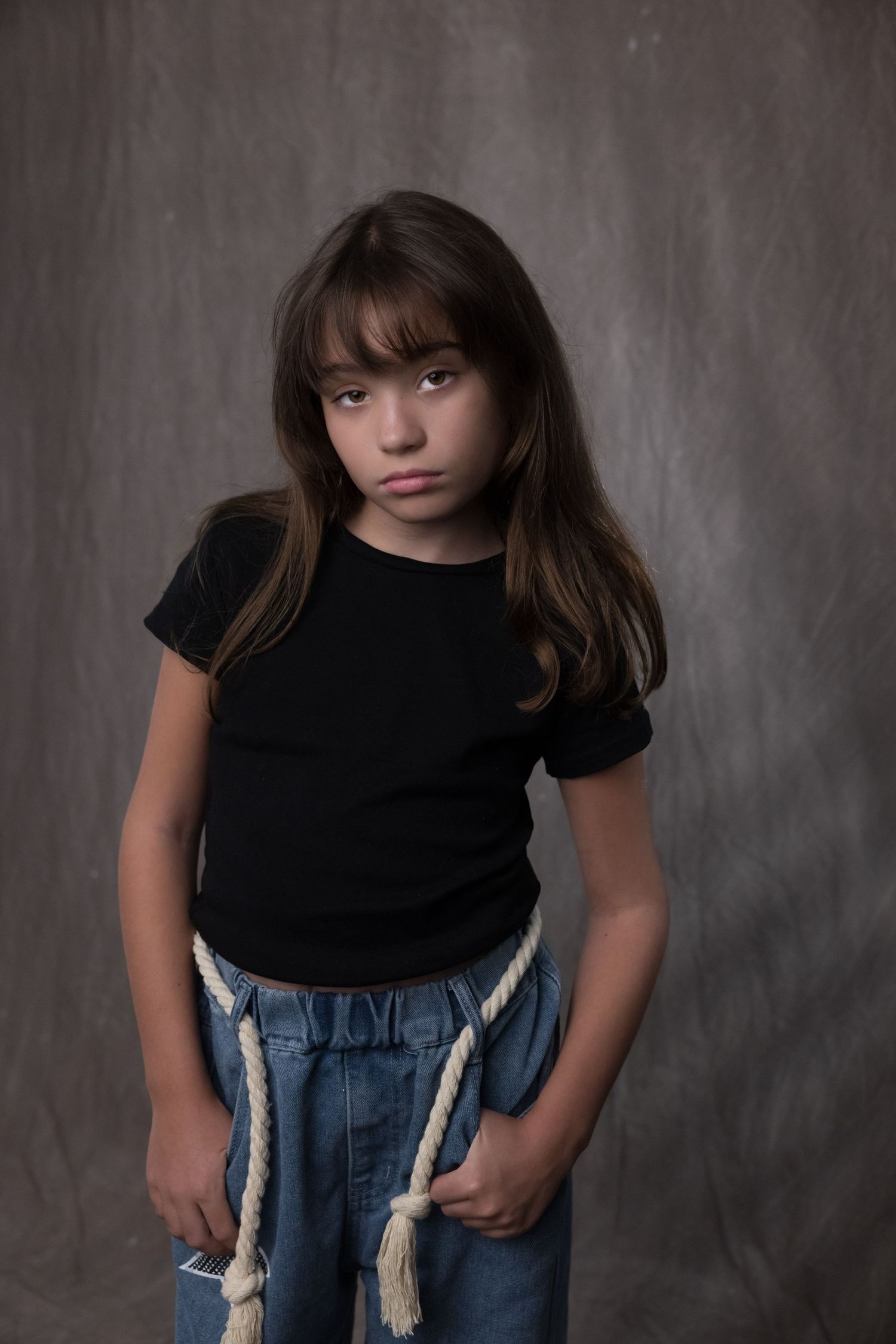 A series of four moody studio portraits showing a young child in a black t-shirt and jeans against a dark background.