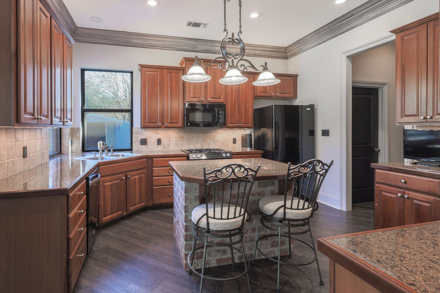 Modern kitchen with cherry wood cabinets, granite countertops, black appliances and wrought iron bar stools at center island.