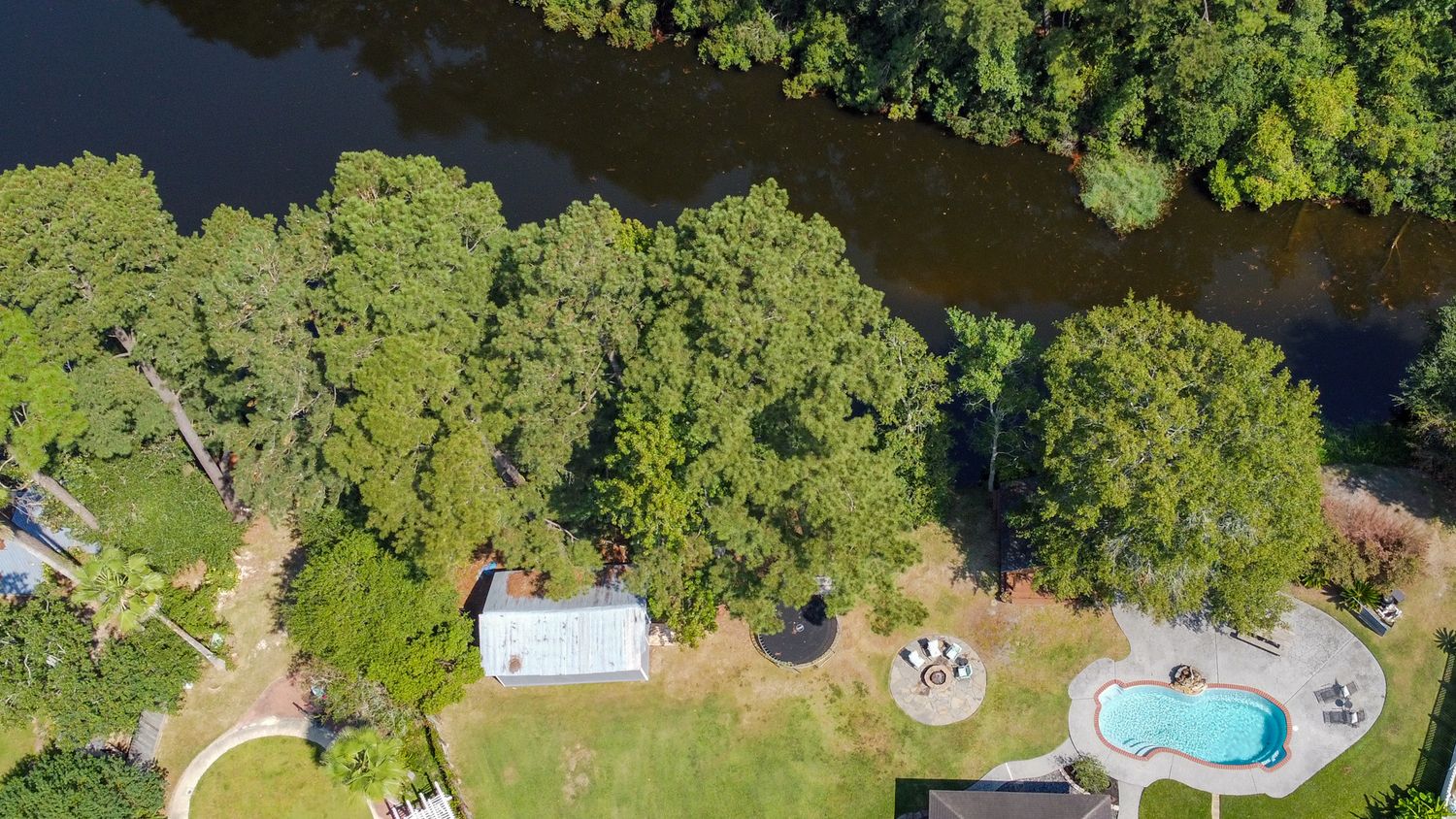 Aerial view of a luxury swimming pool surrounded by lush green trees and landscaping in a residential backyard.