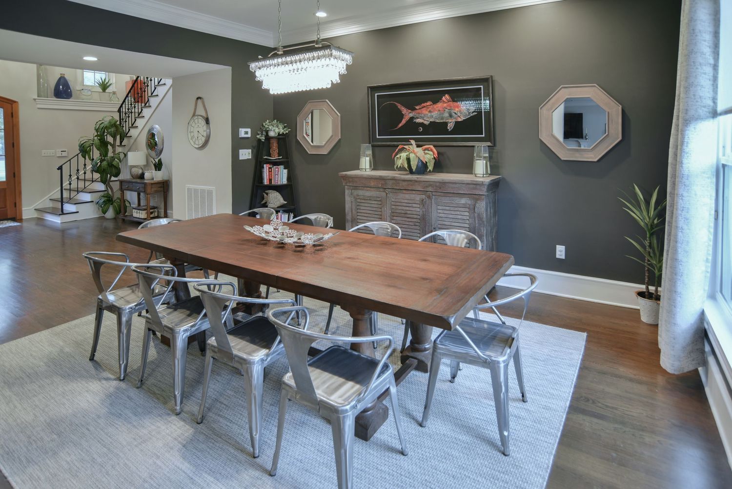 Modern dining room featuring a wood table, metal chairs, gray walls, and circular mirror decor.