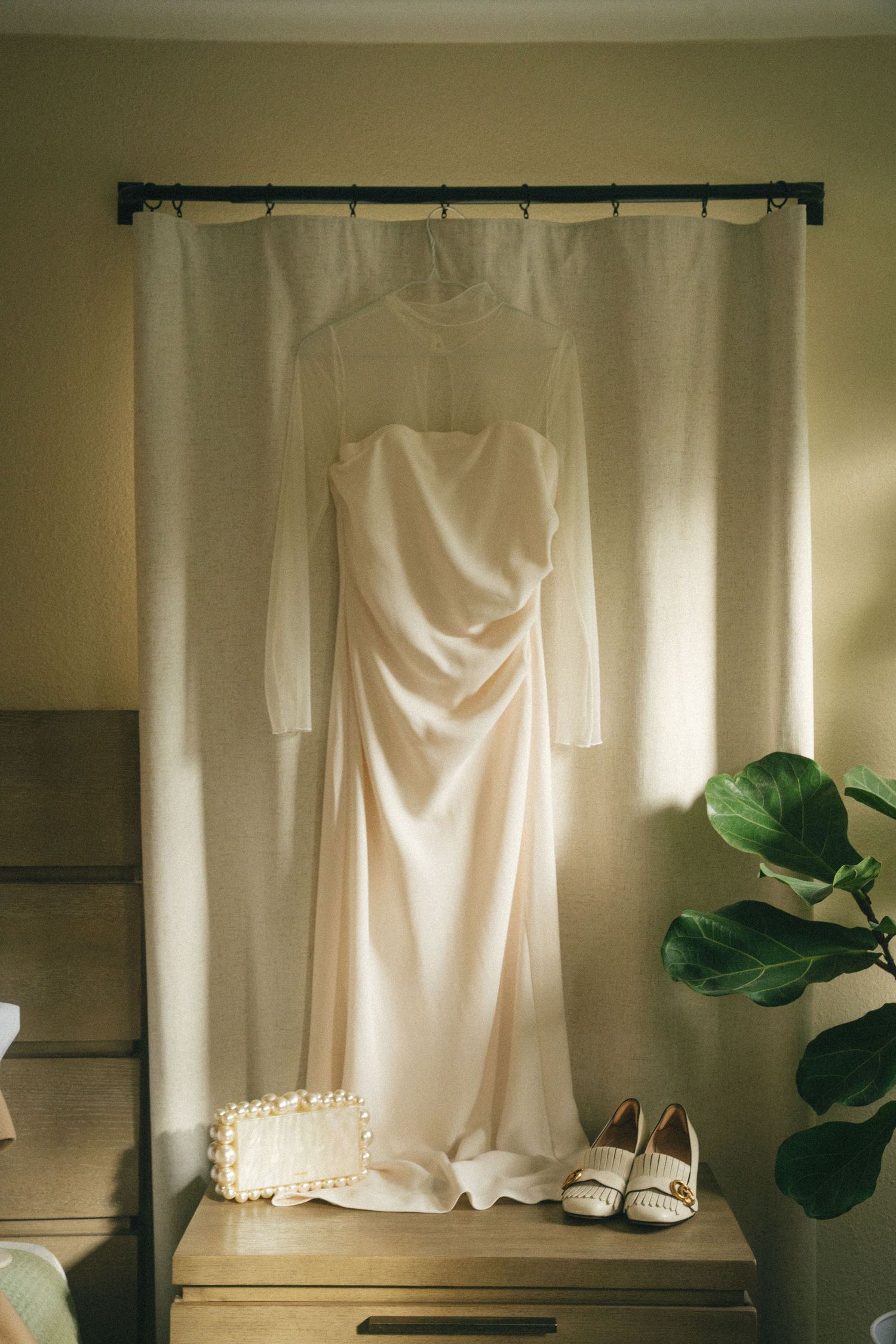Wedding dress and shoes displayed on a curtain rod with soft natural lighting.