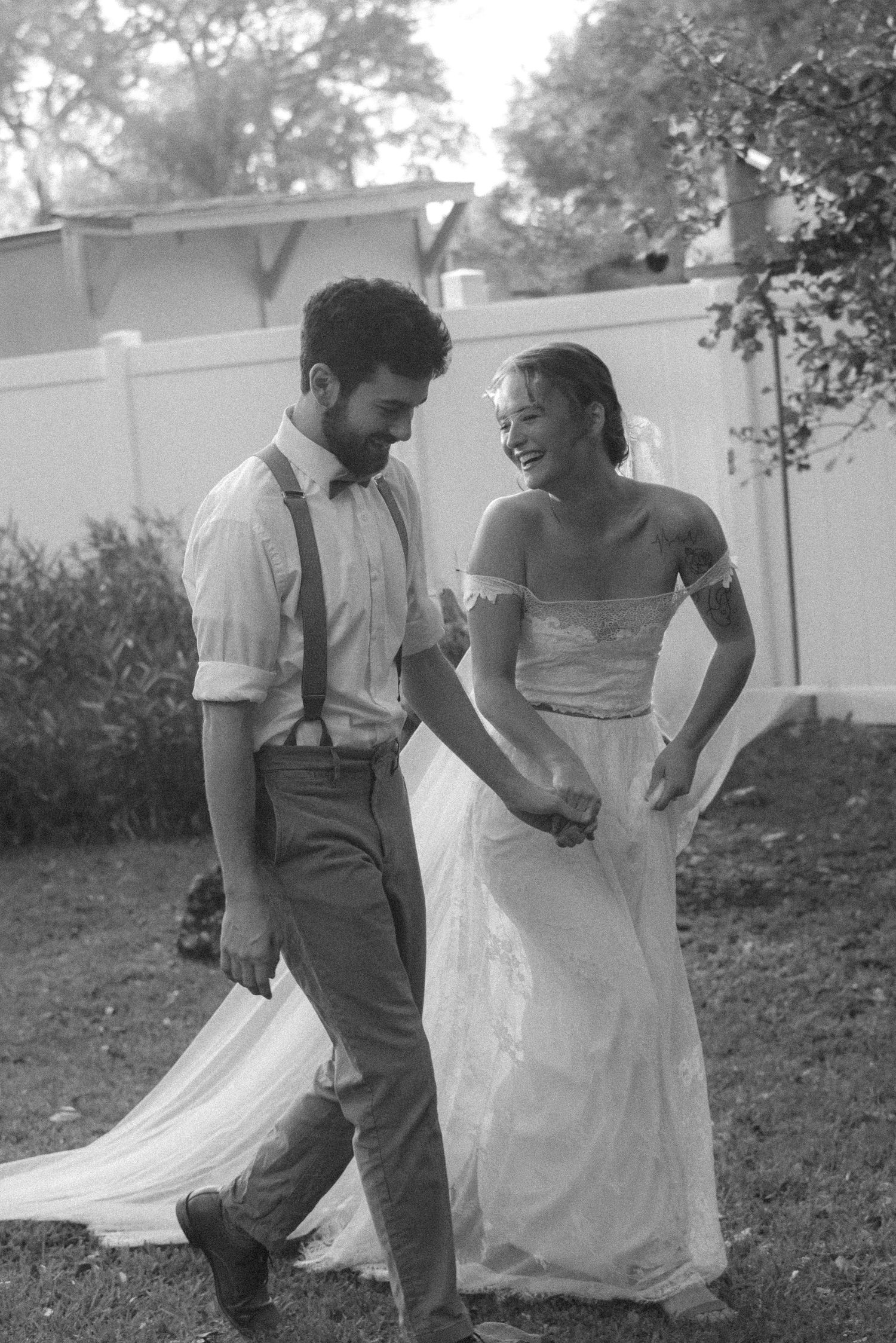 Candid black and white photo of newlyweds sharing a joyful moment in a garden.