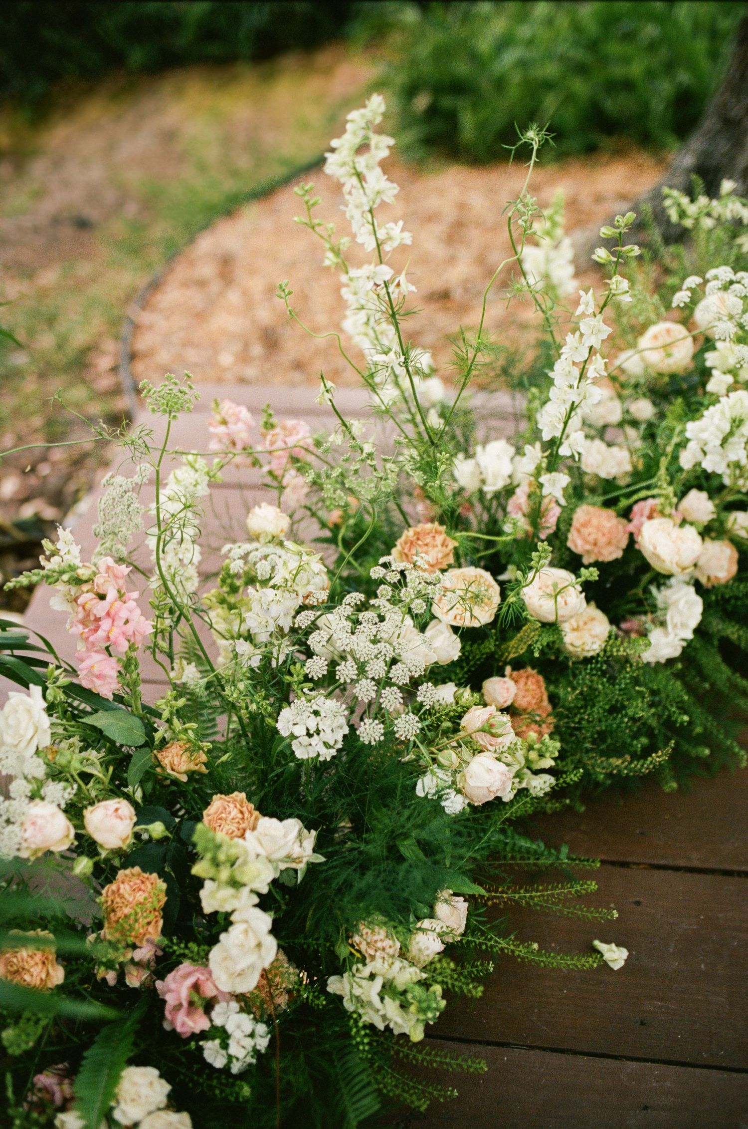 Delicate pink and white flowers arranged along a wooden deck in a garden setting.