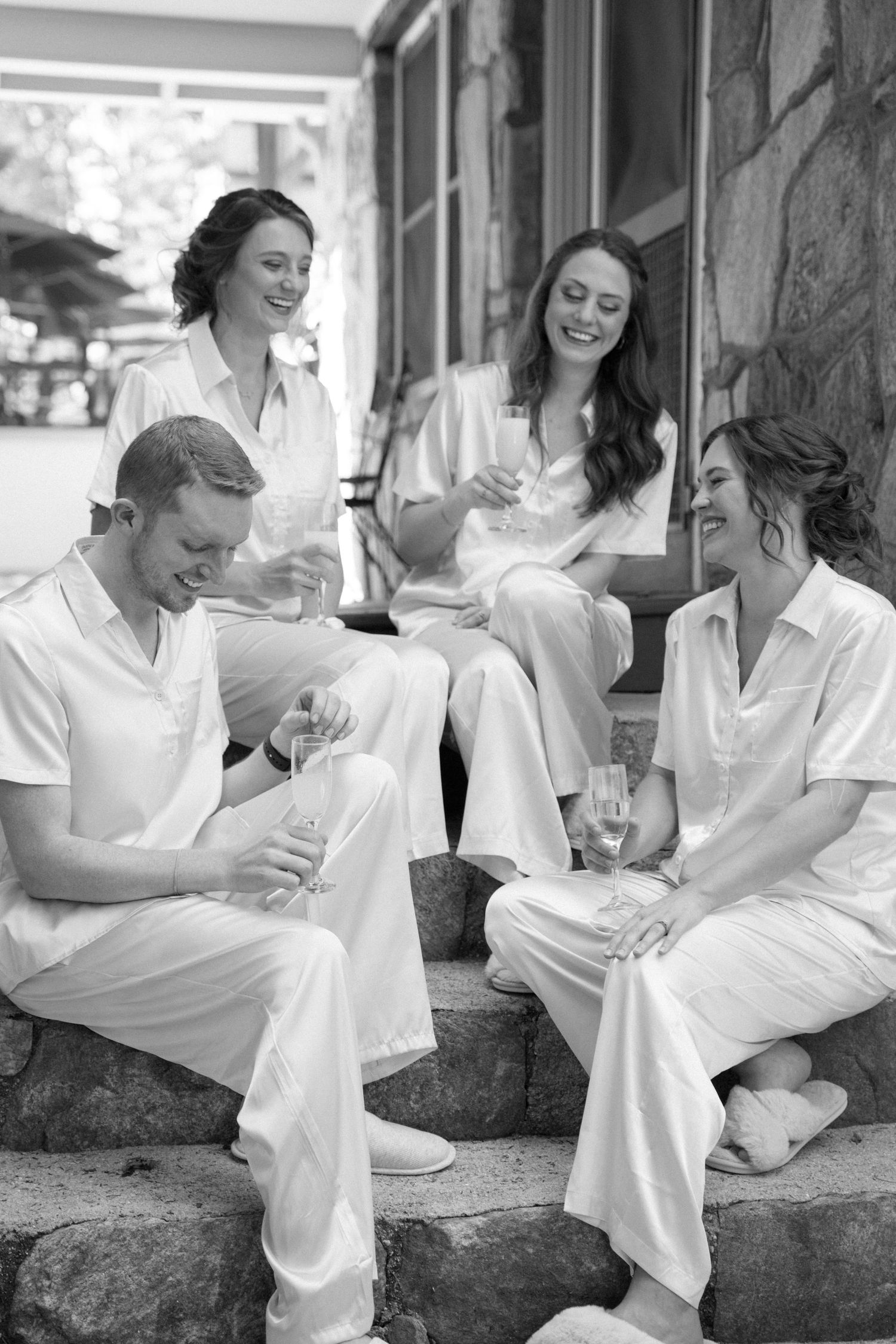 Group in white clothing sharing drinks and laughs on stone steps.