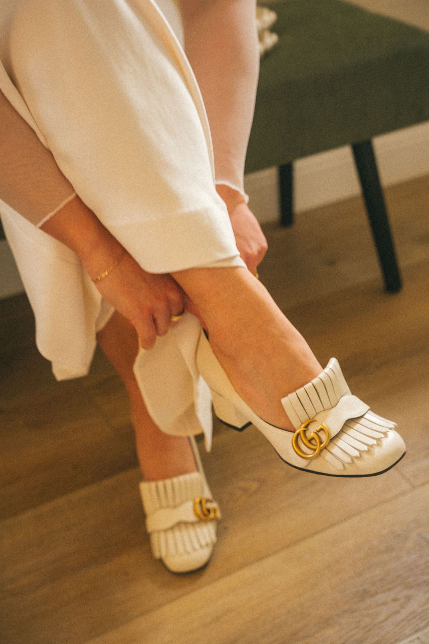 Close-up of vintage-inspired white wedding shoes with gold accents on hardwood floor.