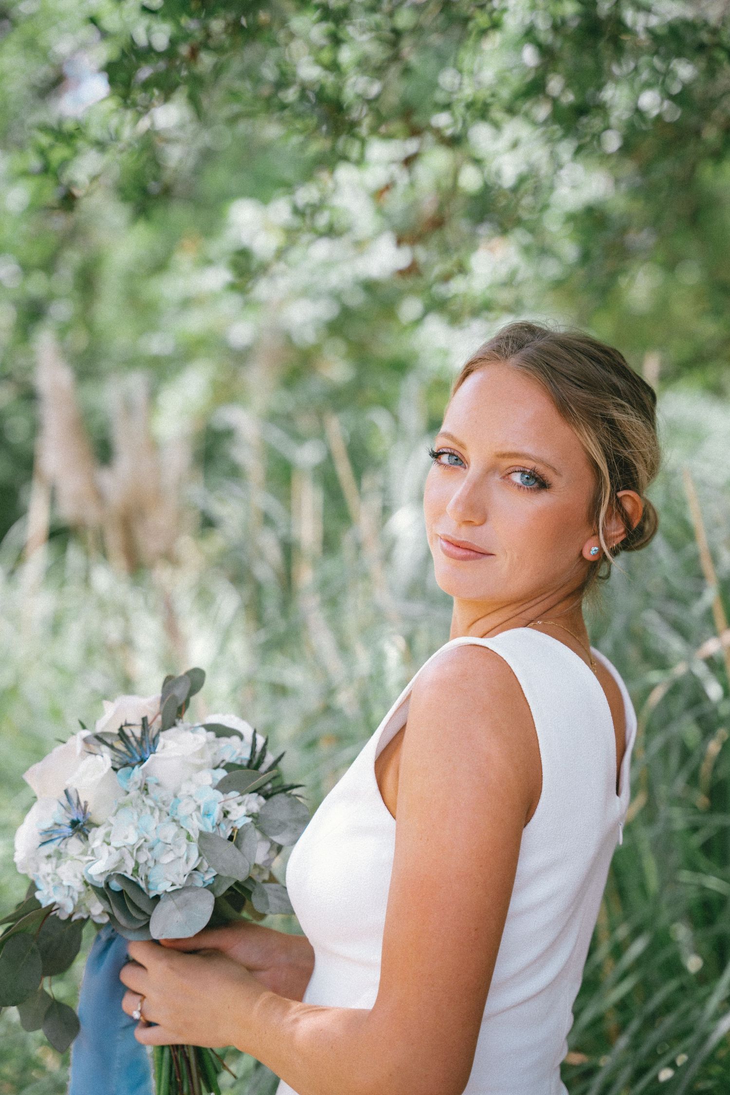 Elegant wedding portrait of a bride with blue and white bouquet against natural garden backdrop.