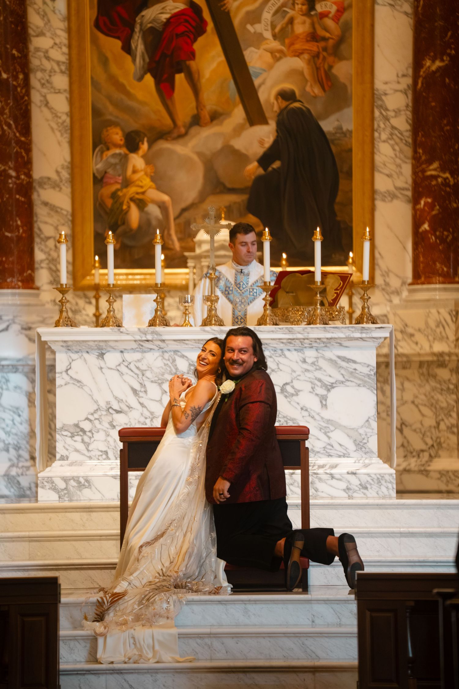 A couple shares a joyful moment in front of marble columns and paintings in an ornate interior setting.