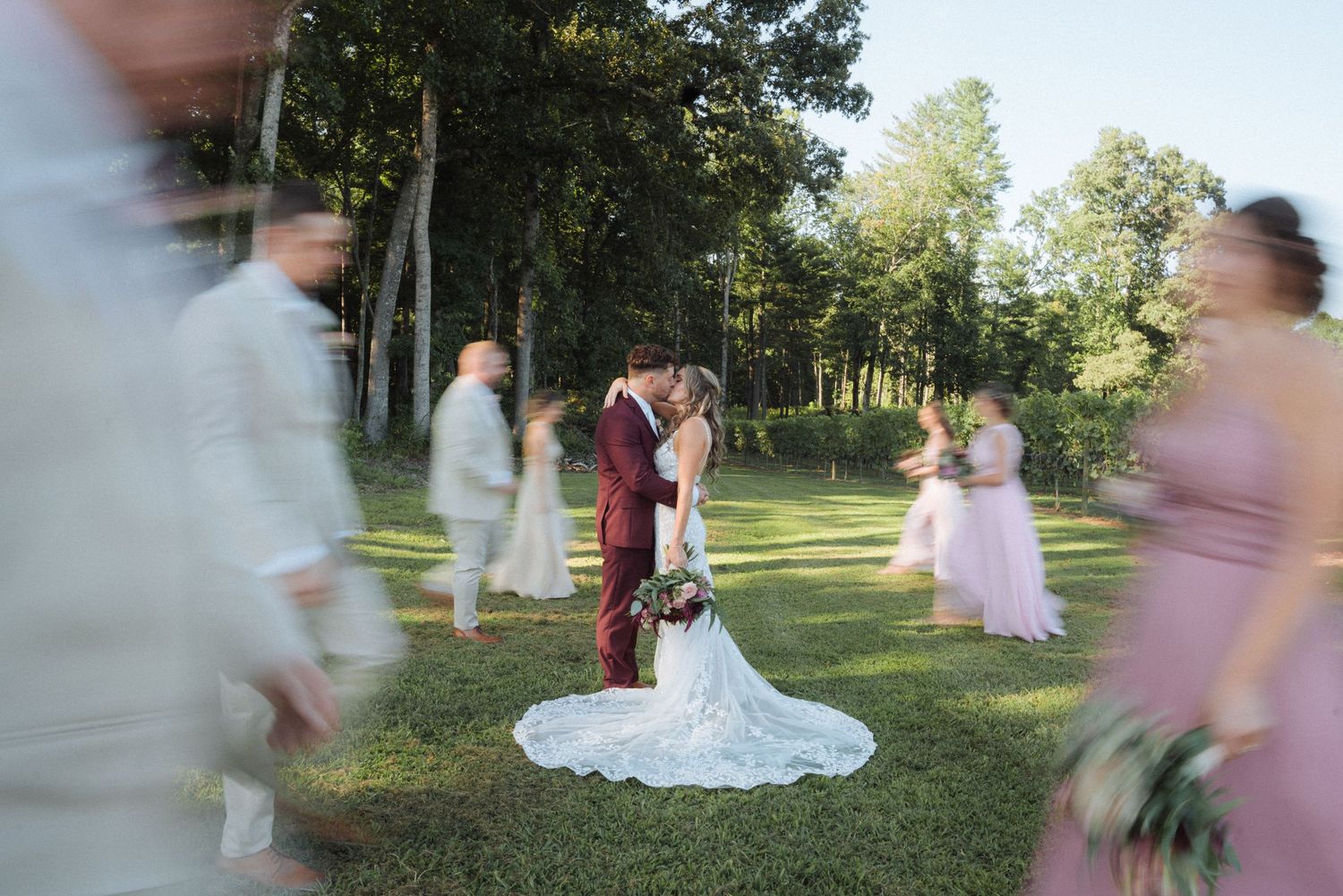 Motion-blurred wedding guests circle around couple during outdoor forest ceremony.