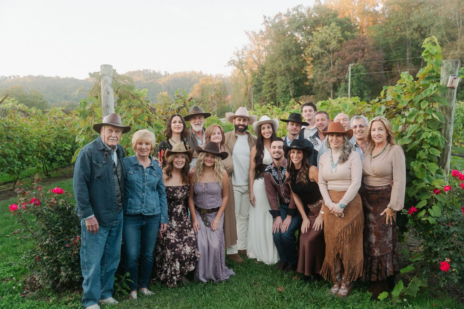 Group of people posing outdoors at a vineyard during golden hour, dressed in bohemian and western attire.