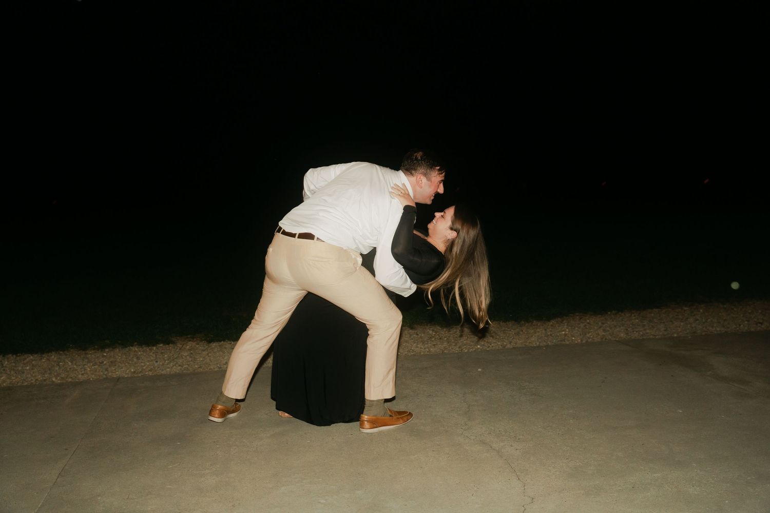 Couple sharing a romantic dip kiss outdoors at night during wedding celebration.