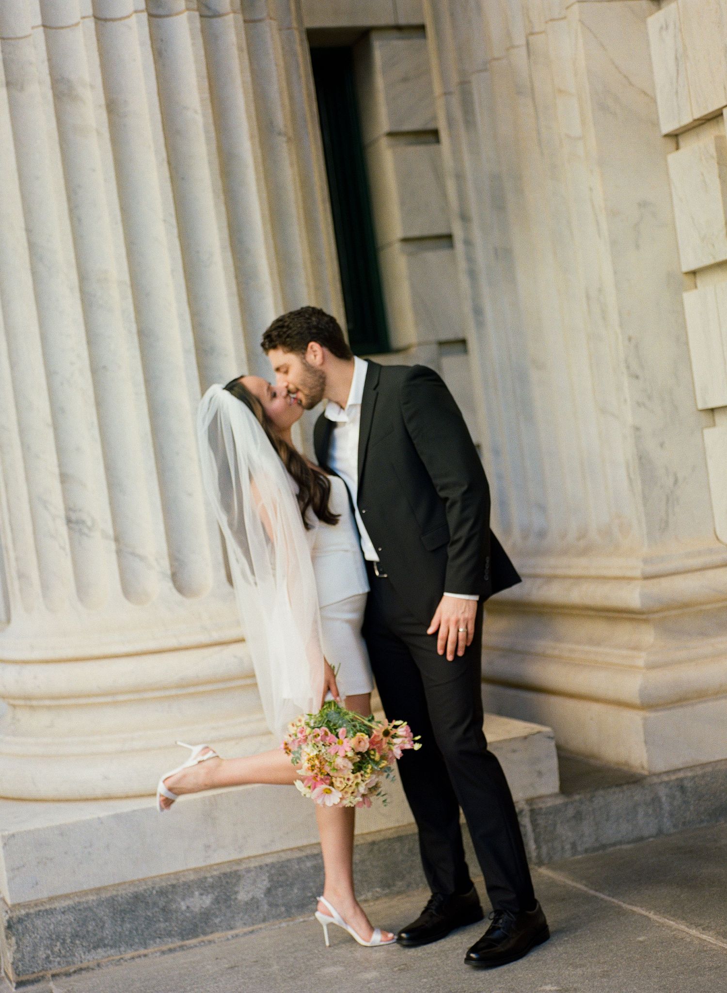 Romantic couple poses by classical white marble columns.