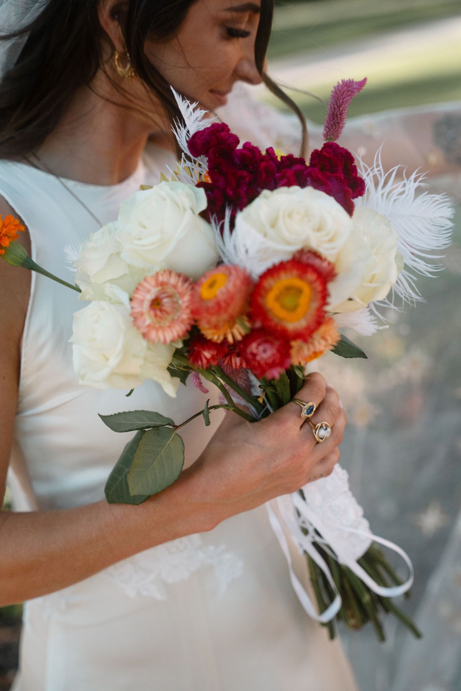 A bridal bouquet features vibrant red and white flowers with delicate feather accents.