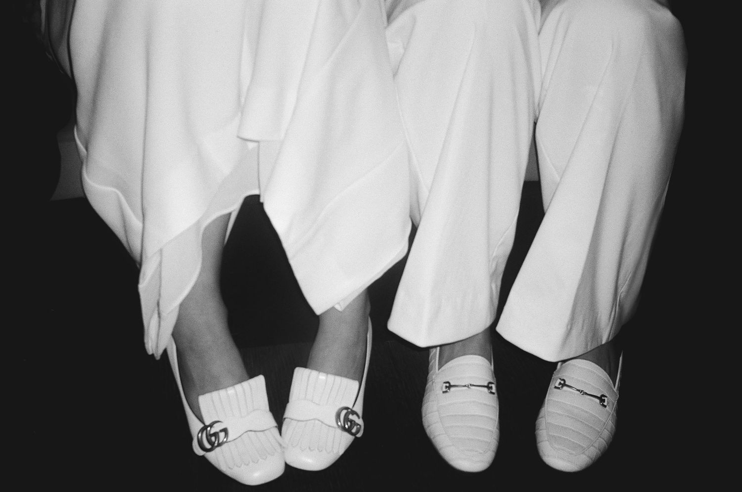 Detail shot of white wedding shoes and dresses in black and white photography.