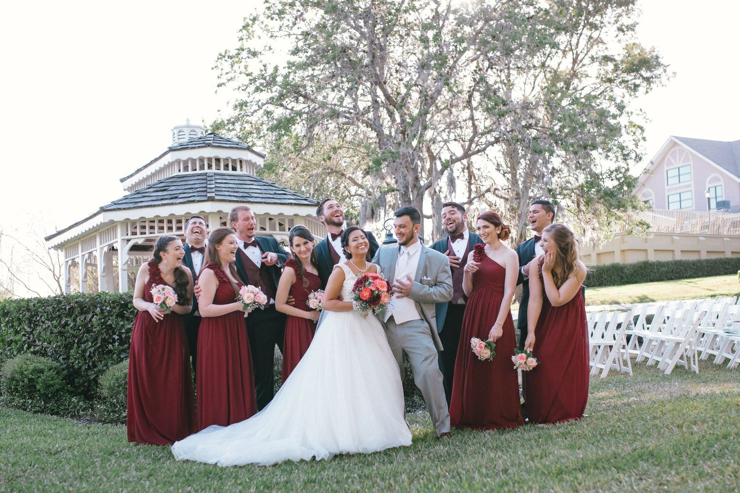 Wedding party in burgundy dresses and suits poses together on a lawn.