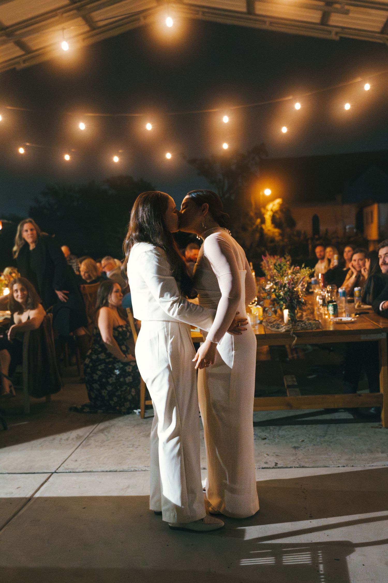 Wedding reception under a tent with string lights and guests celebrating at decorated tables.