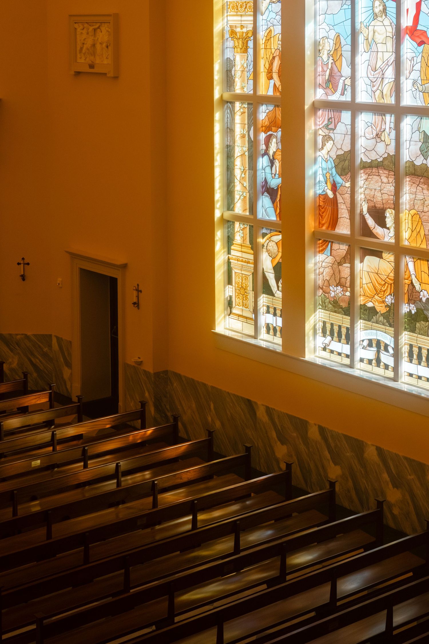 Sunlight streams through stained glass windows onto empty wooden church pews.