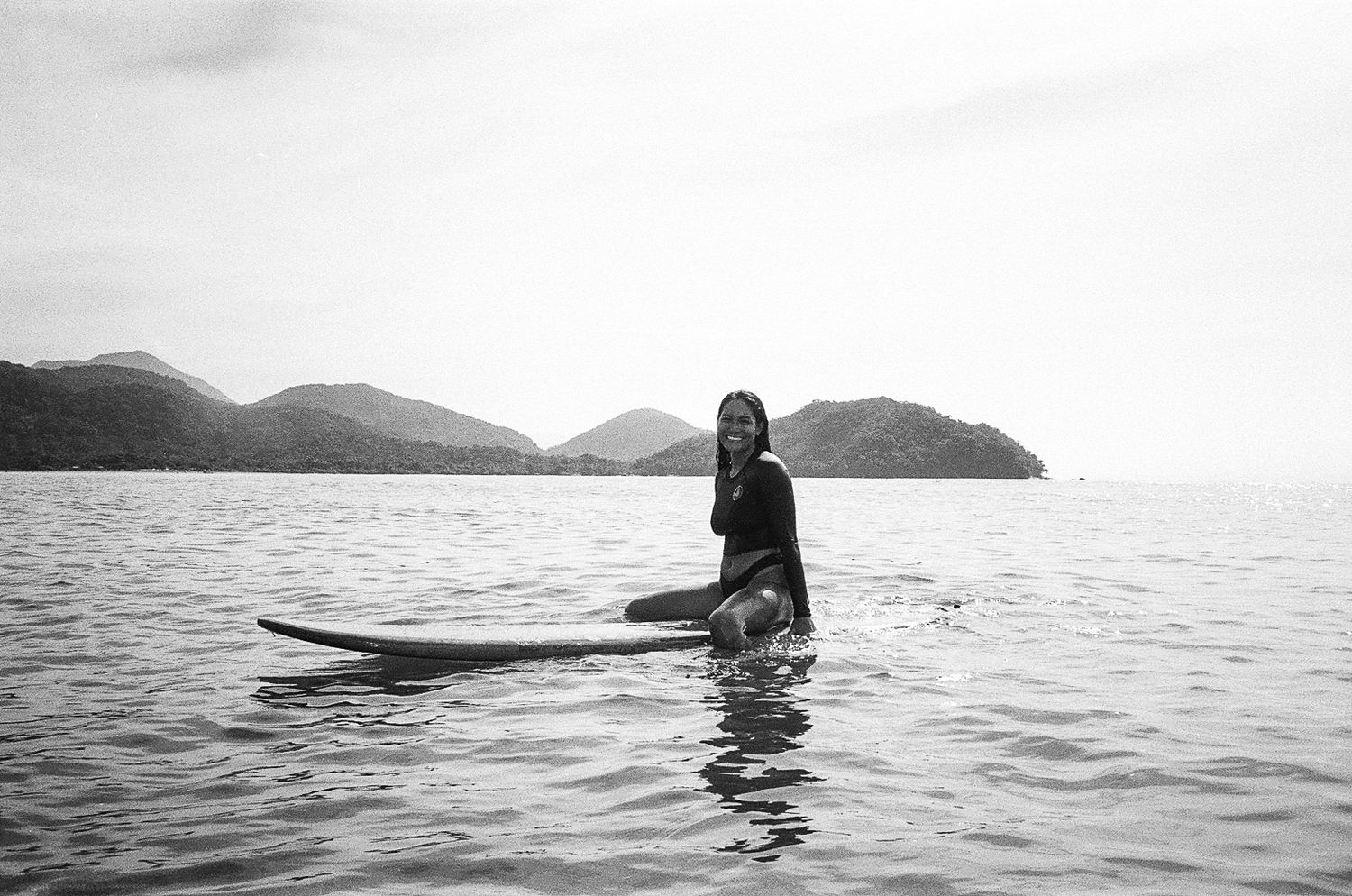Person paddling on surfboard in peaceful waters near mountainous coastline in Brazil.
