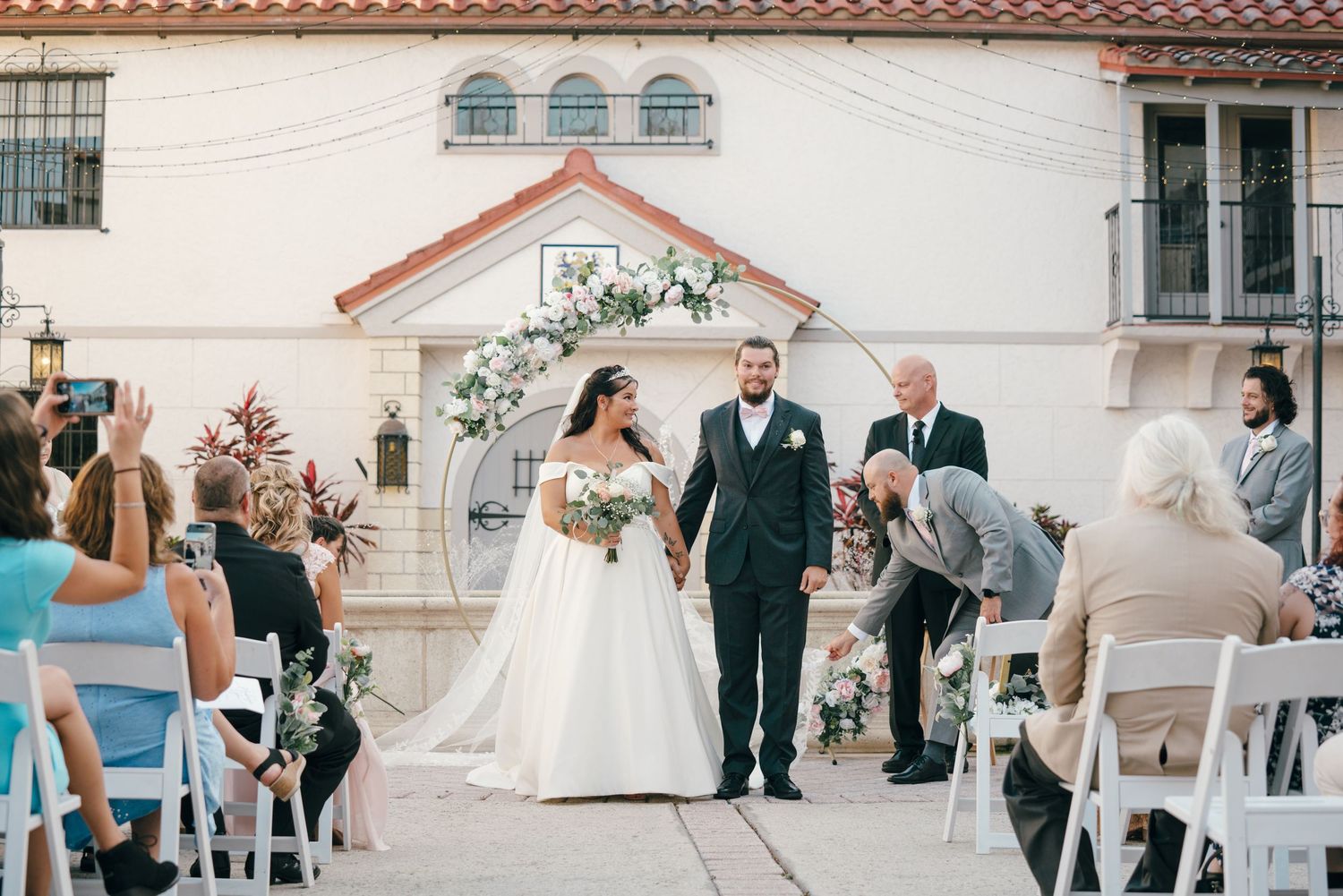 Outdoor wedding ceremony setup with Mediterranean-style architecture and white decor.