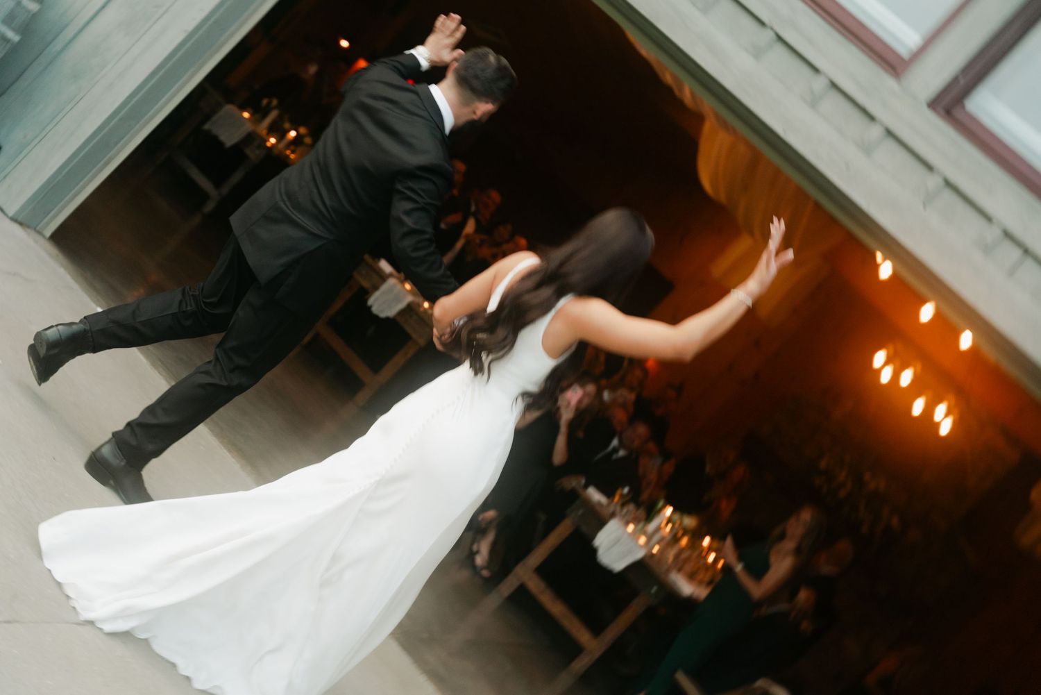 Bride and groom share their first dance at a romantic wedding reception with warm candlelight and guests watching.