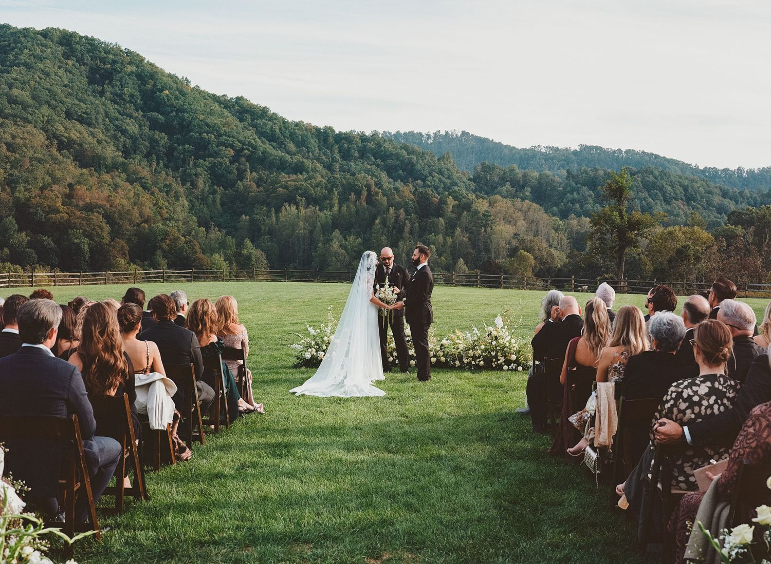 Bride and groom exchange vows at outdoor wedding ceremony with stunning mountain backdrop and wooded hills.