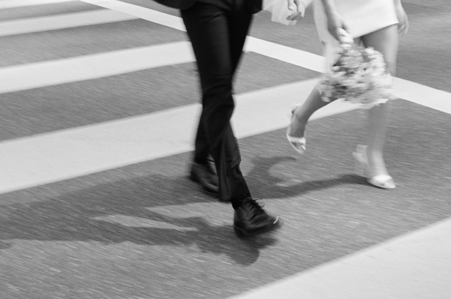 Black and white photo of pedestrians crossing a zebra crossing, motion blur capturing dynamic urban street scene.