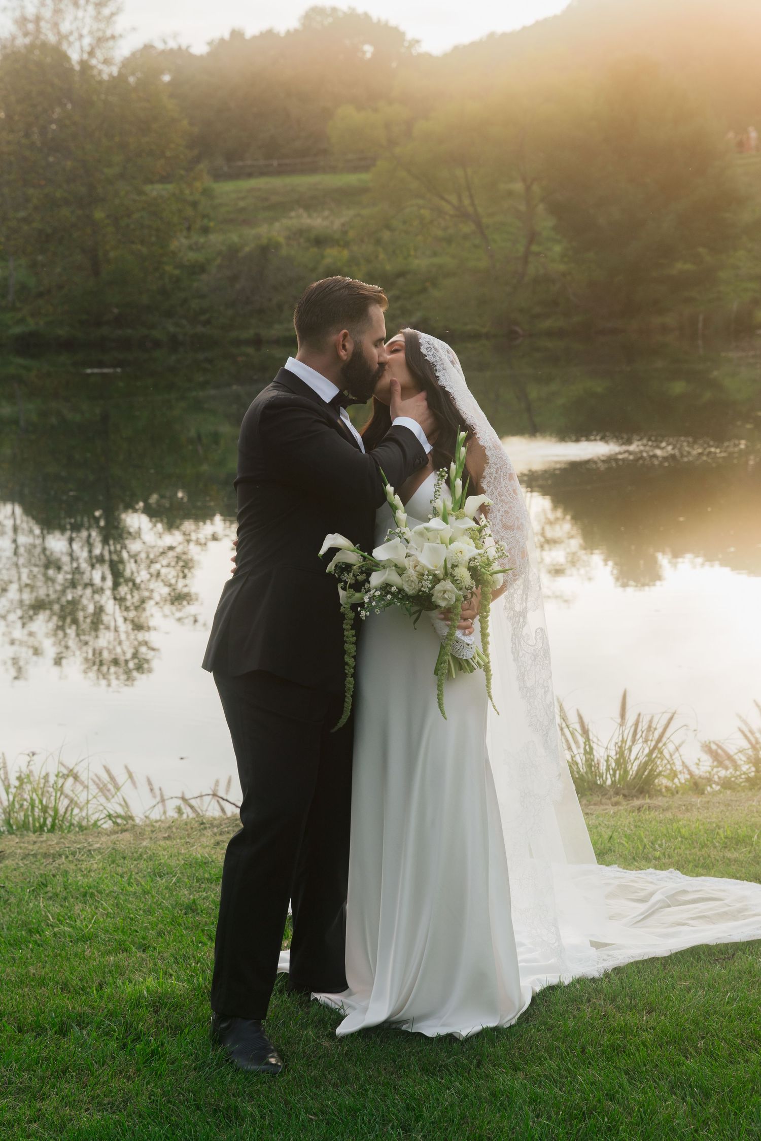 Sunset wedding portrait by a reflective pond with lush greenery in the background.