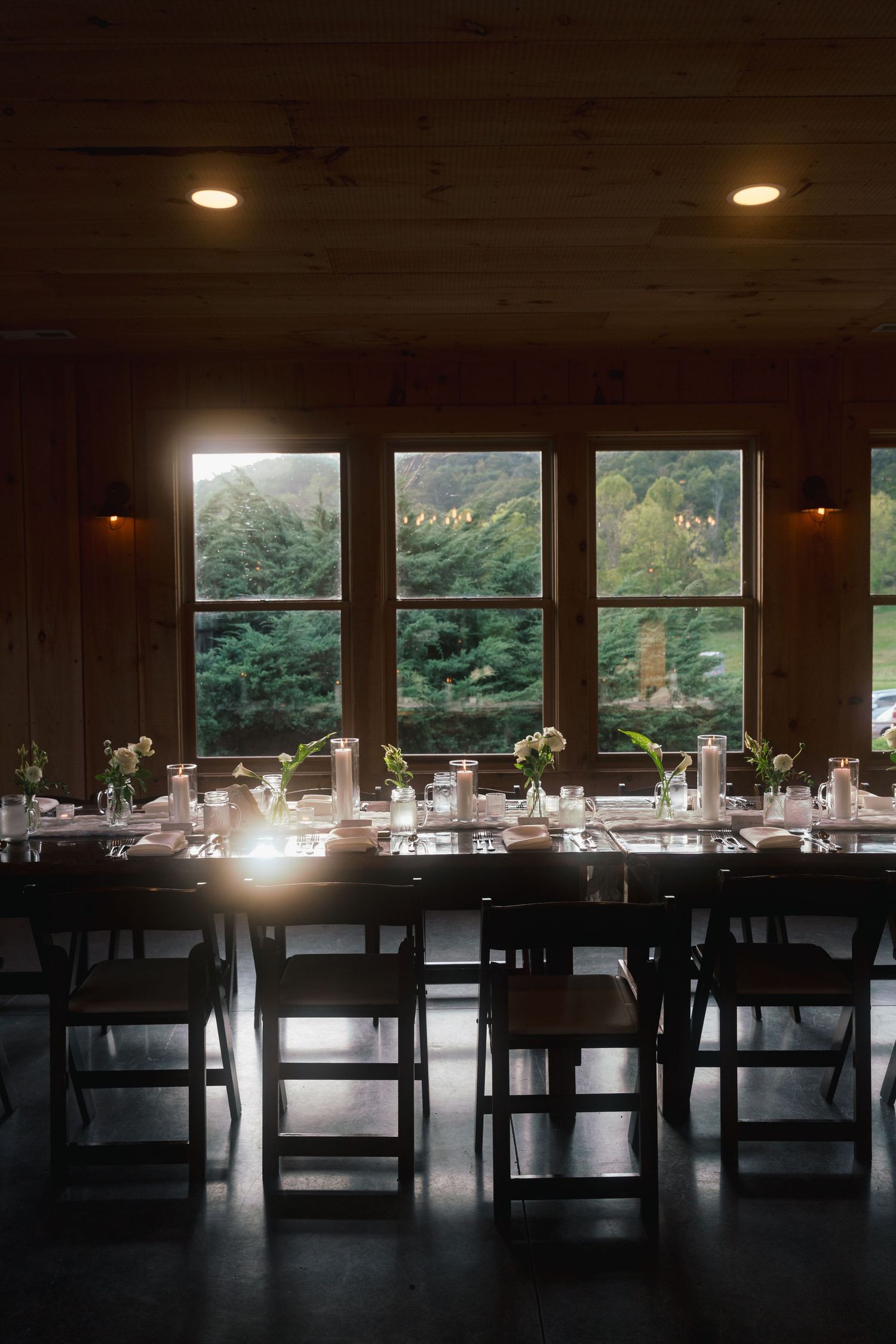 Elegant wedding reception table setup in a rustic venue with large windows overlooking mountains.