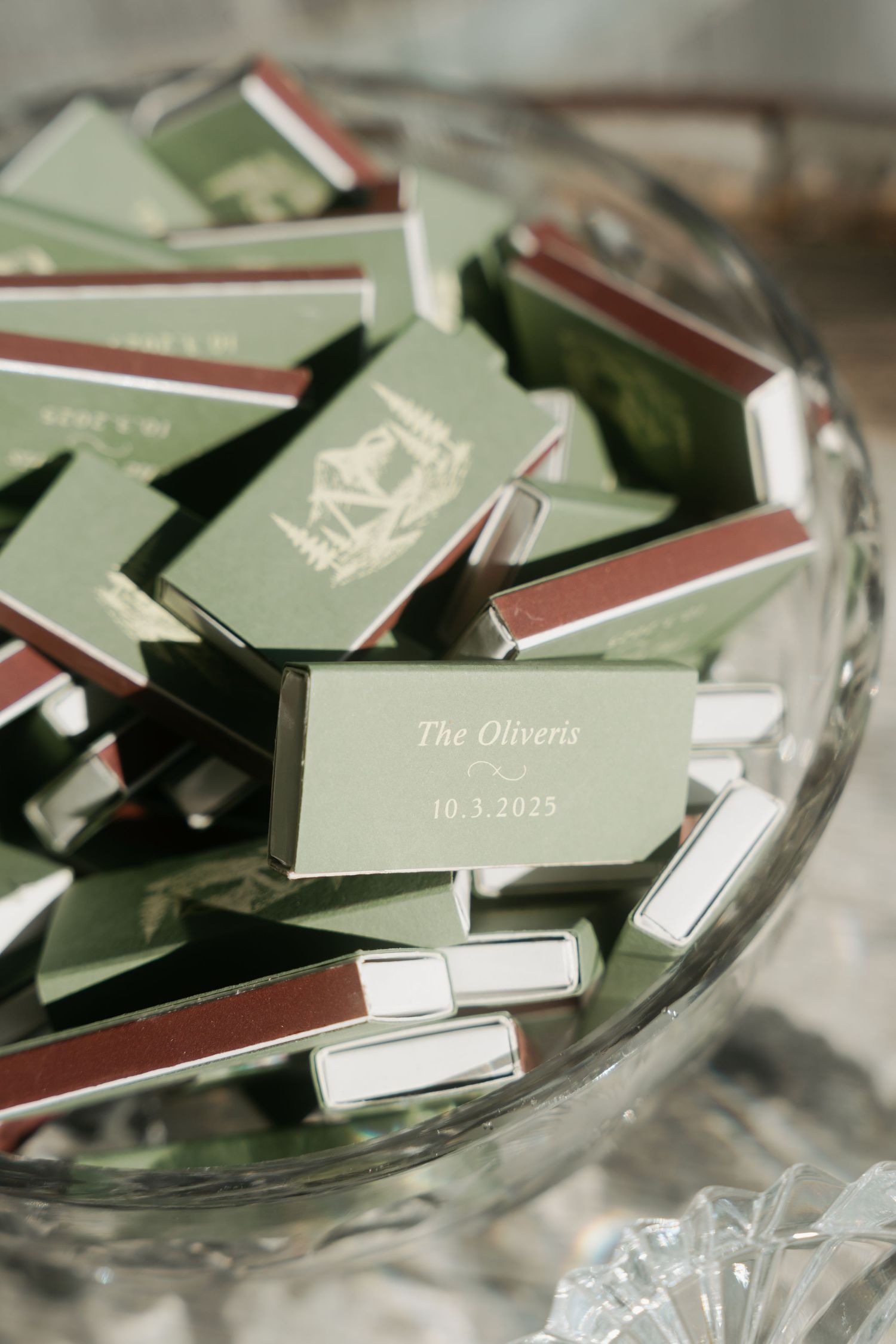 Green matchboxes personalized for The Oliverts wedding on 10.3.2023 displayed in a crystal bowl.