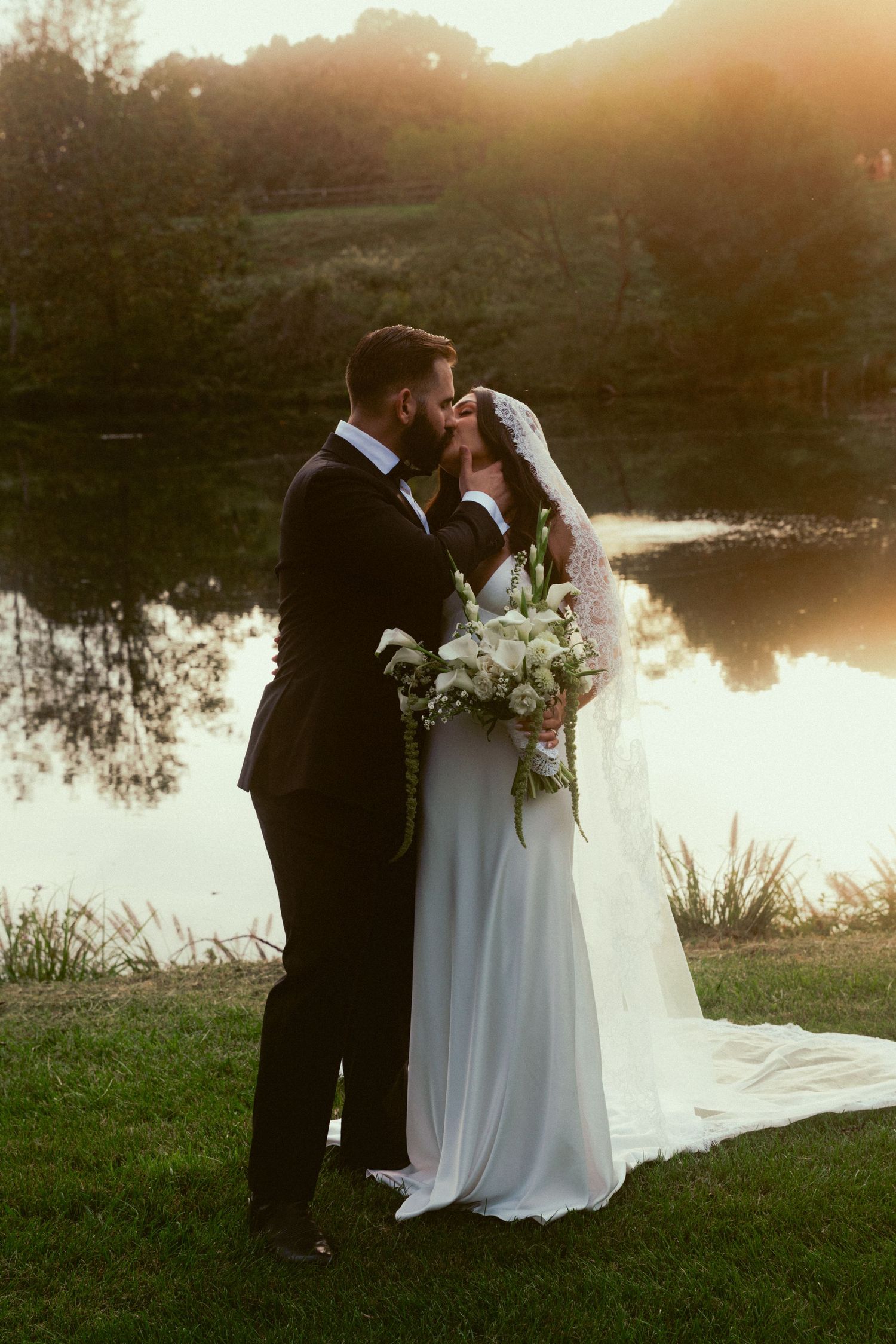 A romantic sunset wedding photoshoot by a serene lake with the couple in formal attire.