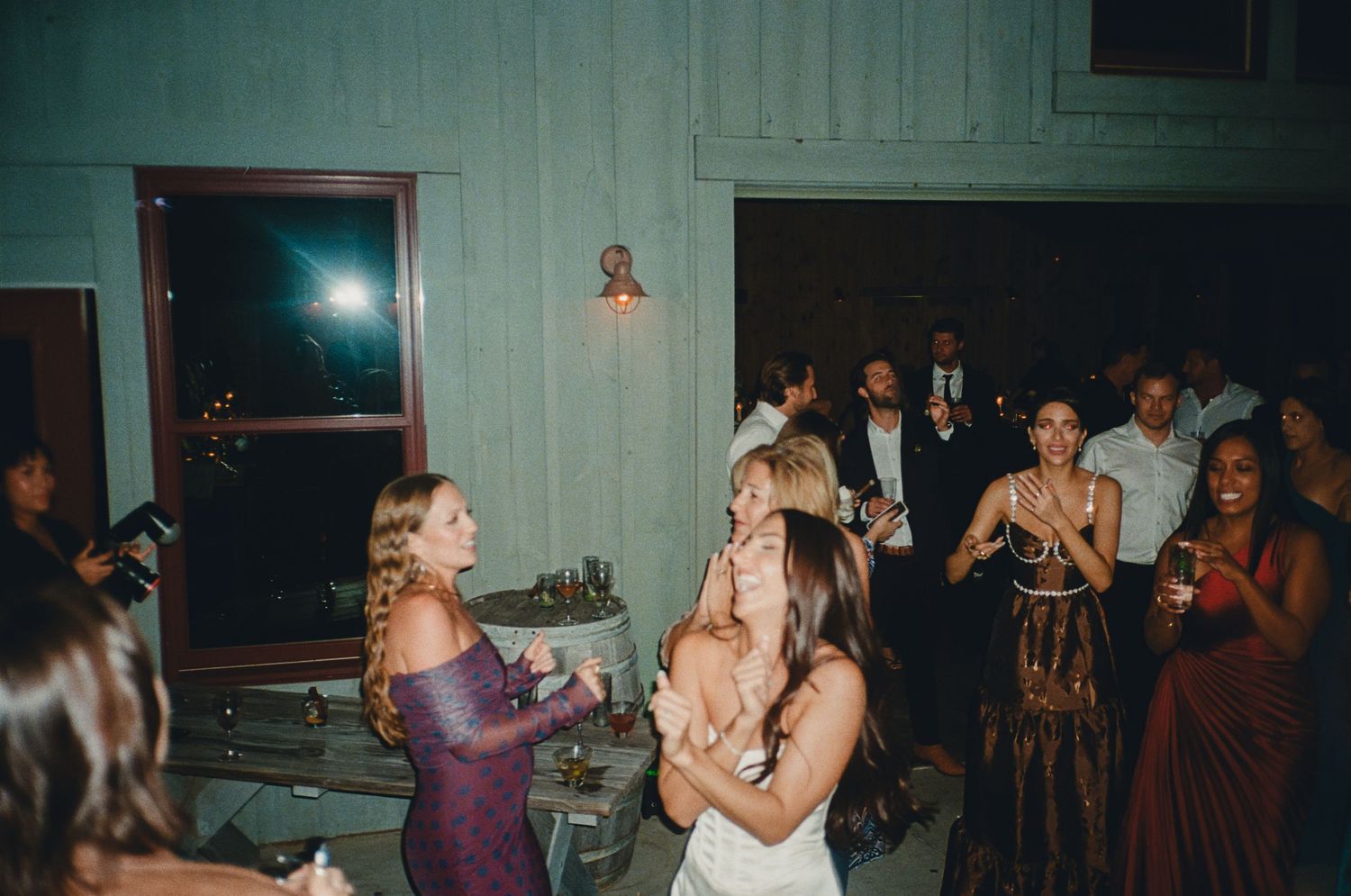 Wedding guests dancing and celebrating on a dimly lit reception dance floor.