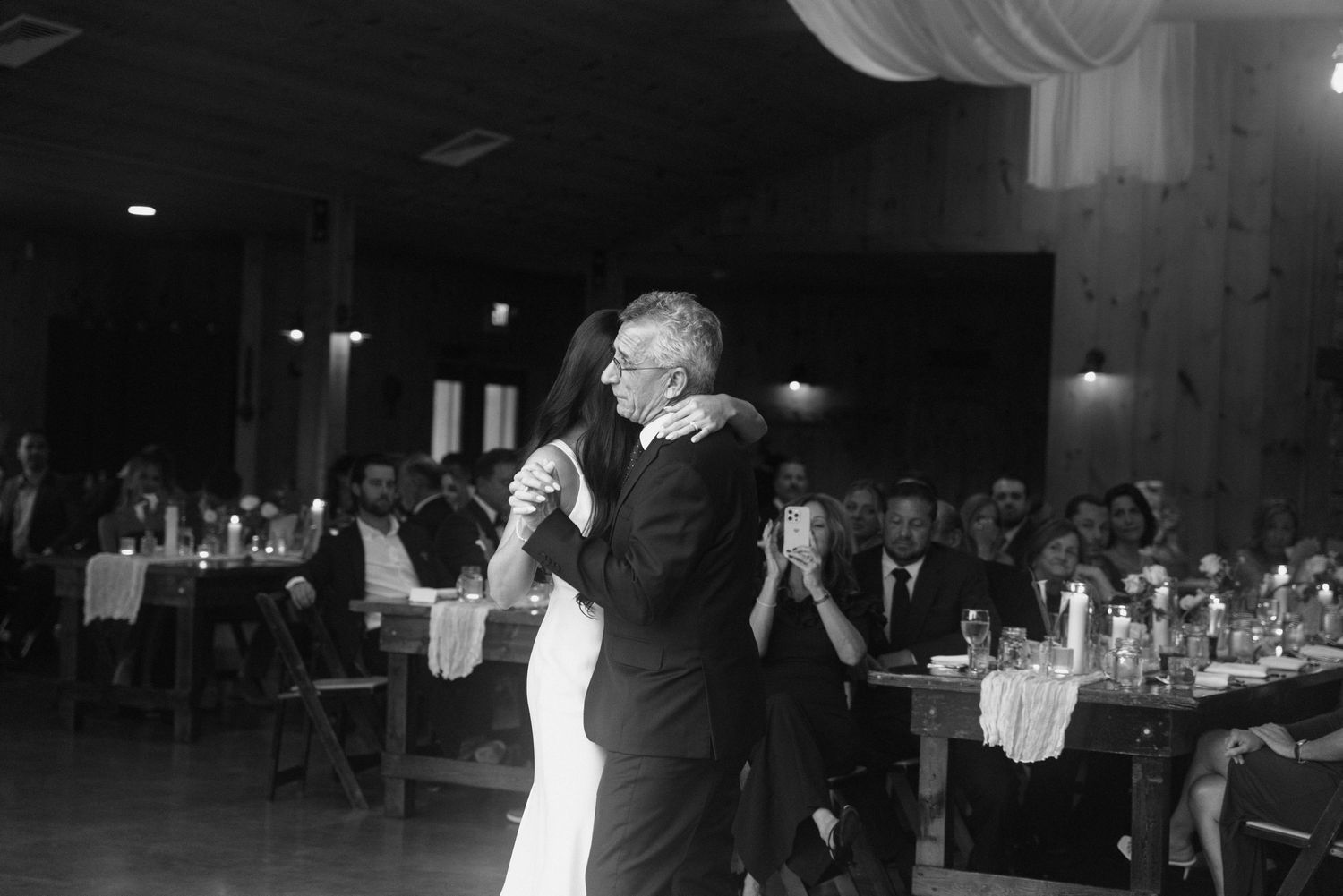 Bride and groom share their first dance at a rustic wedding reception in black and white photo.