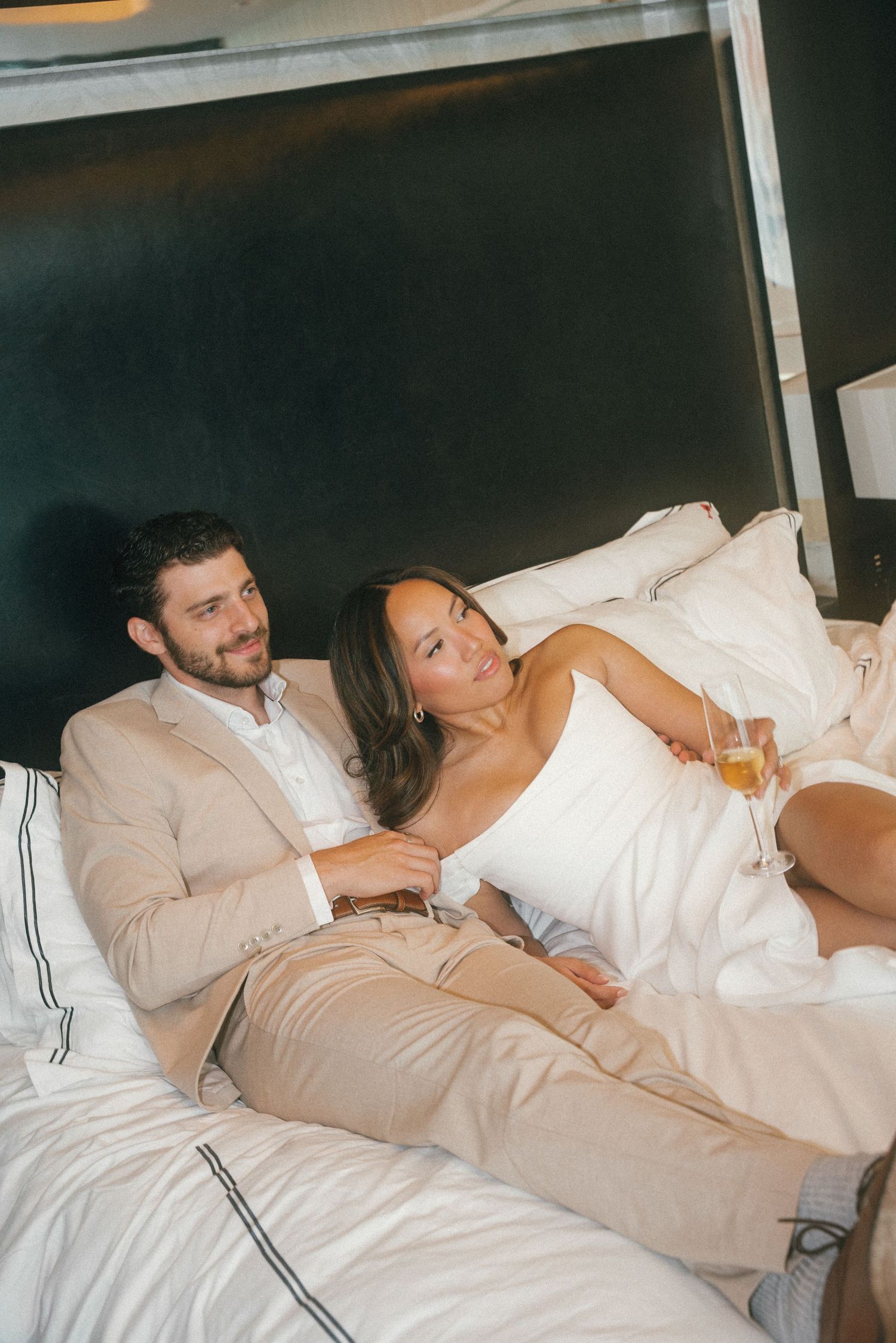 Two people lounging in white bedding while having a casual conversation.