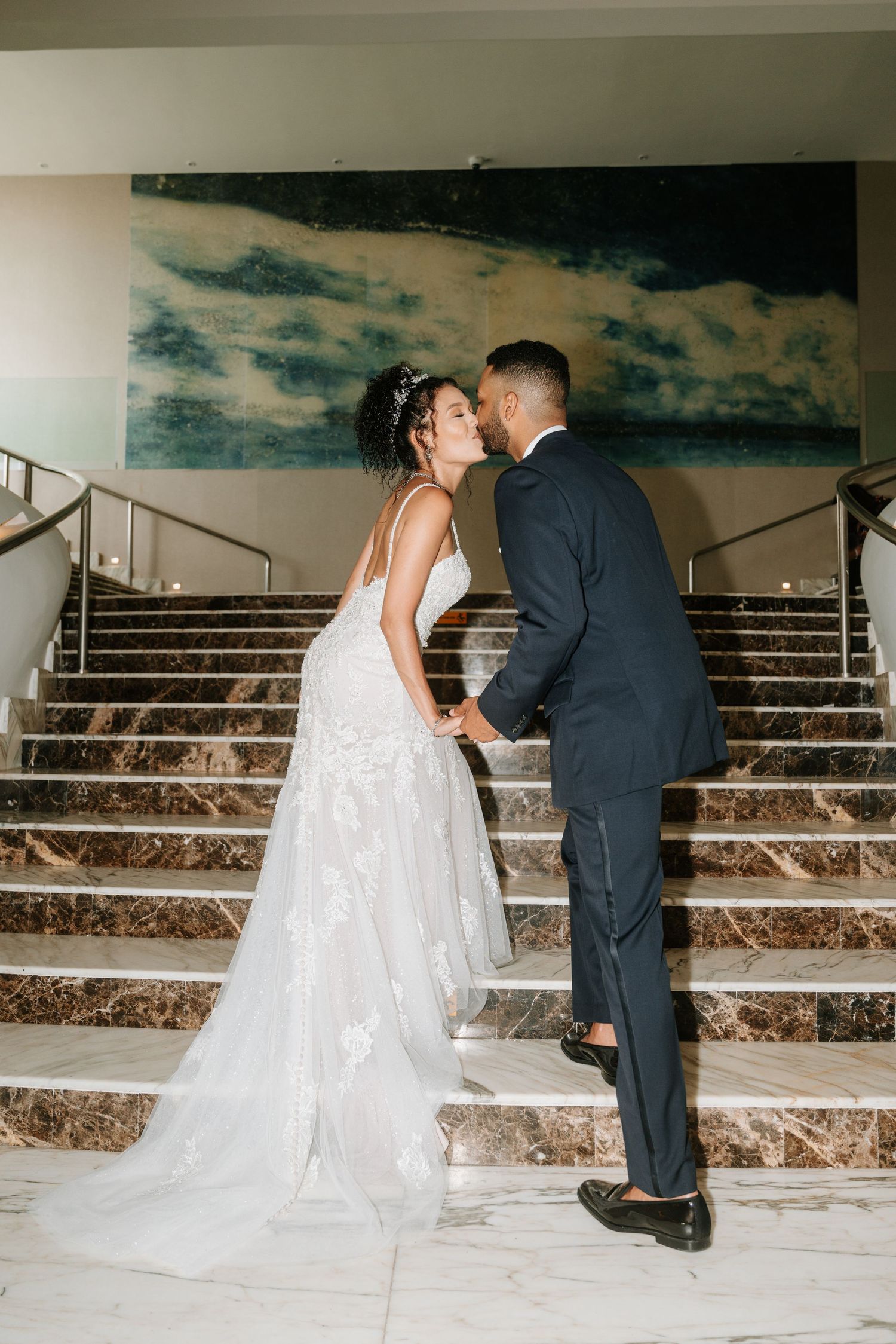 Wedding couple ascending stone steps with dramatic lighting and cloudy backdrop.