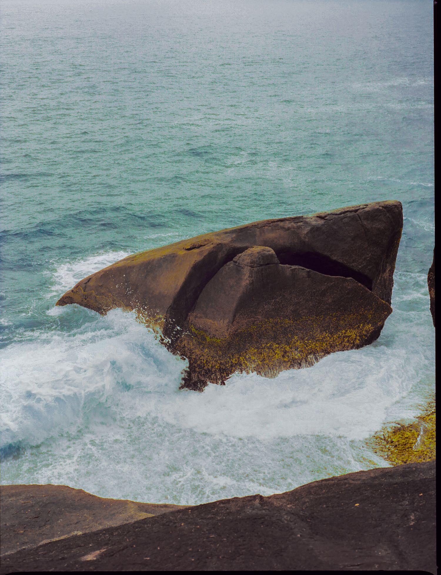 Waves crashing against rocky coastal outcrop with turquoise ocean waters.