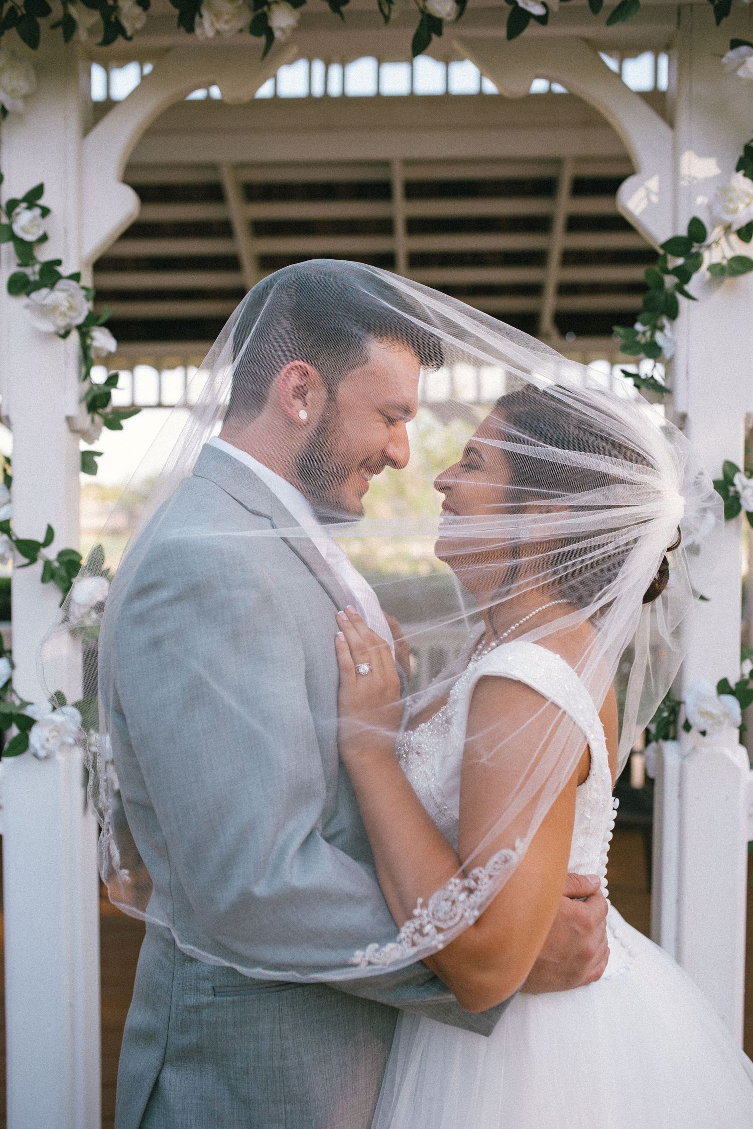 Newlyweds share a romantic moment under a gazebo decorated with white flowers.