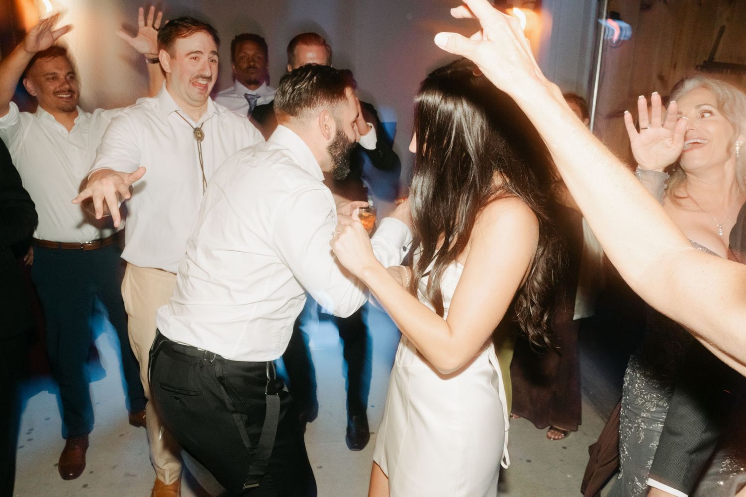 Bride and groom dancing joyfully with wedding guests at lively reception party.