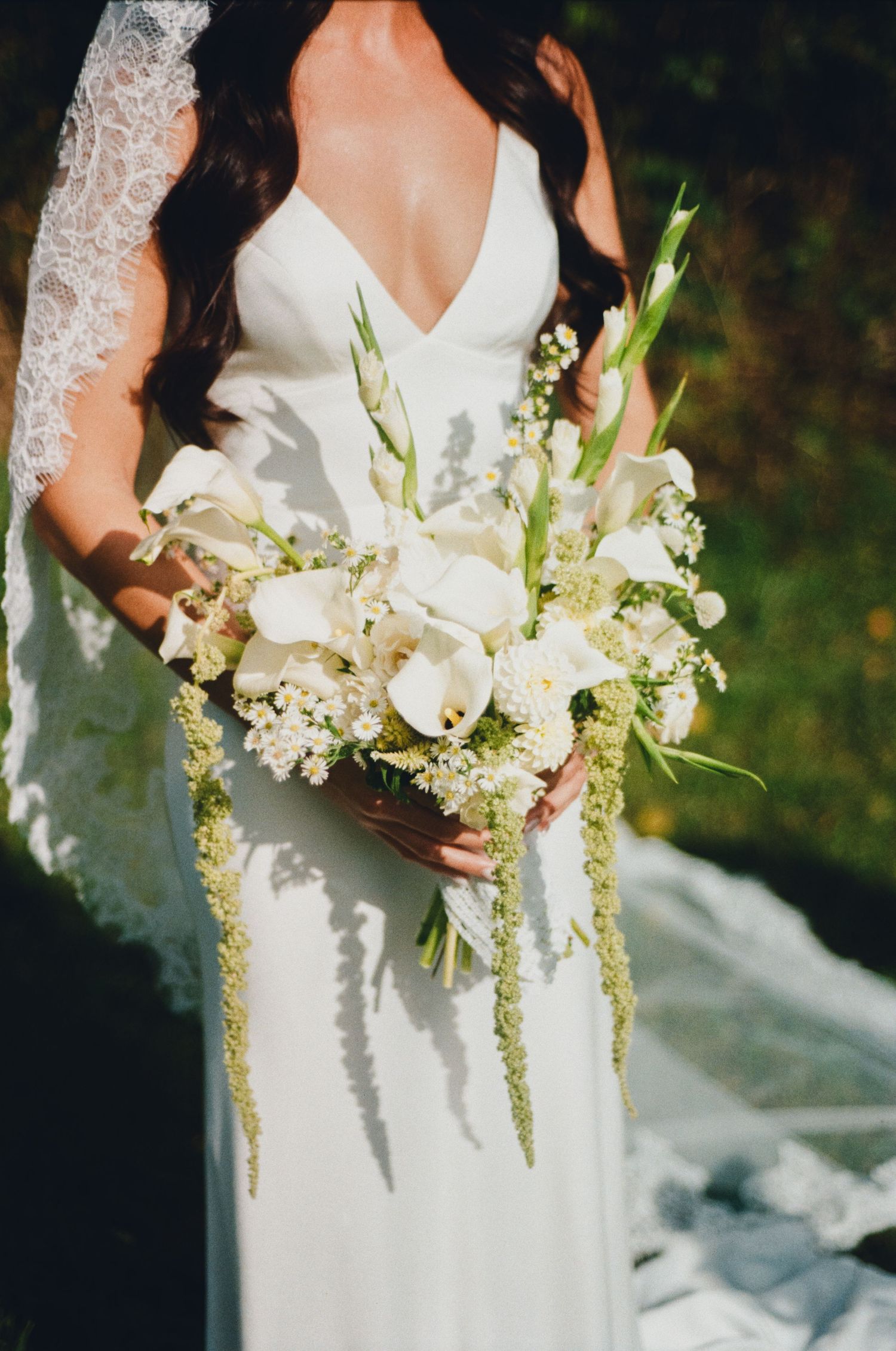 Bride in white lace wedding gown holding elegant bouquet of white calla lilies and green amaranthus.