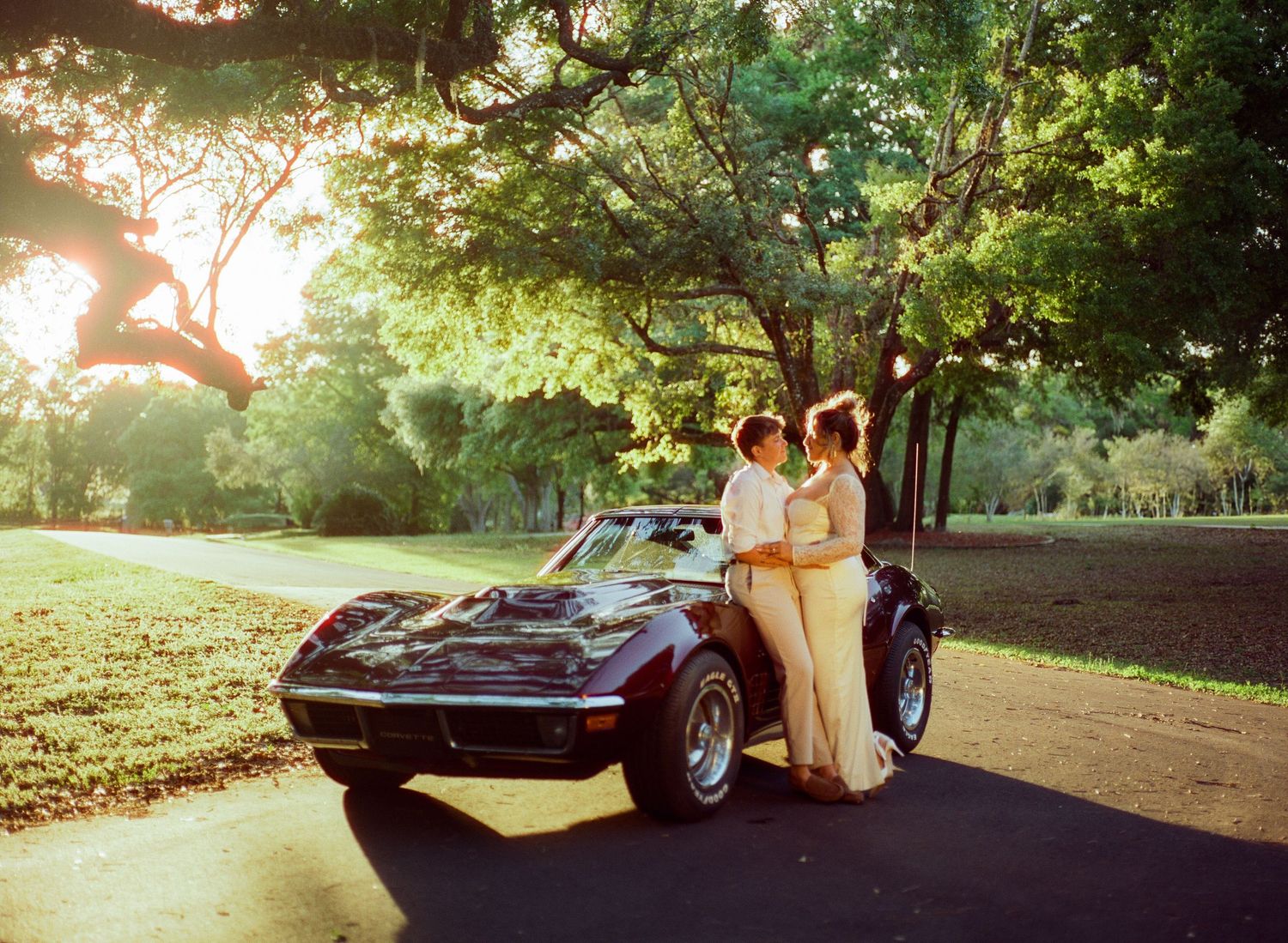 Classic convertible car parked on a tree-lined road during golden hour sunset.