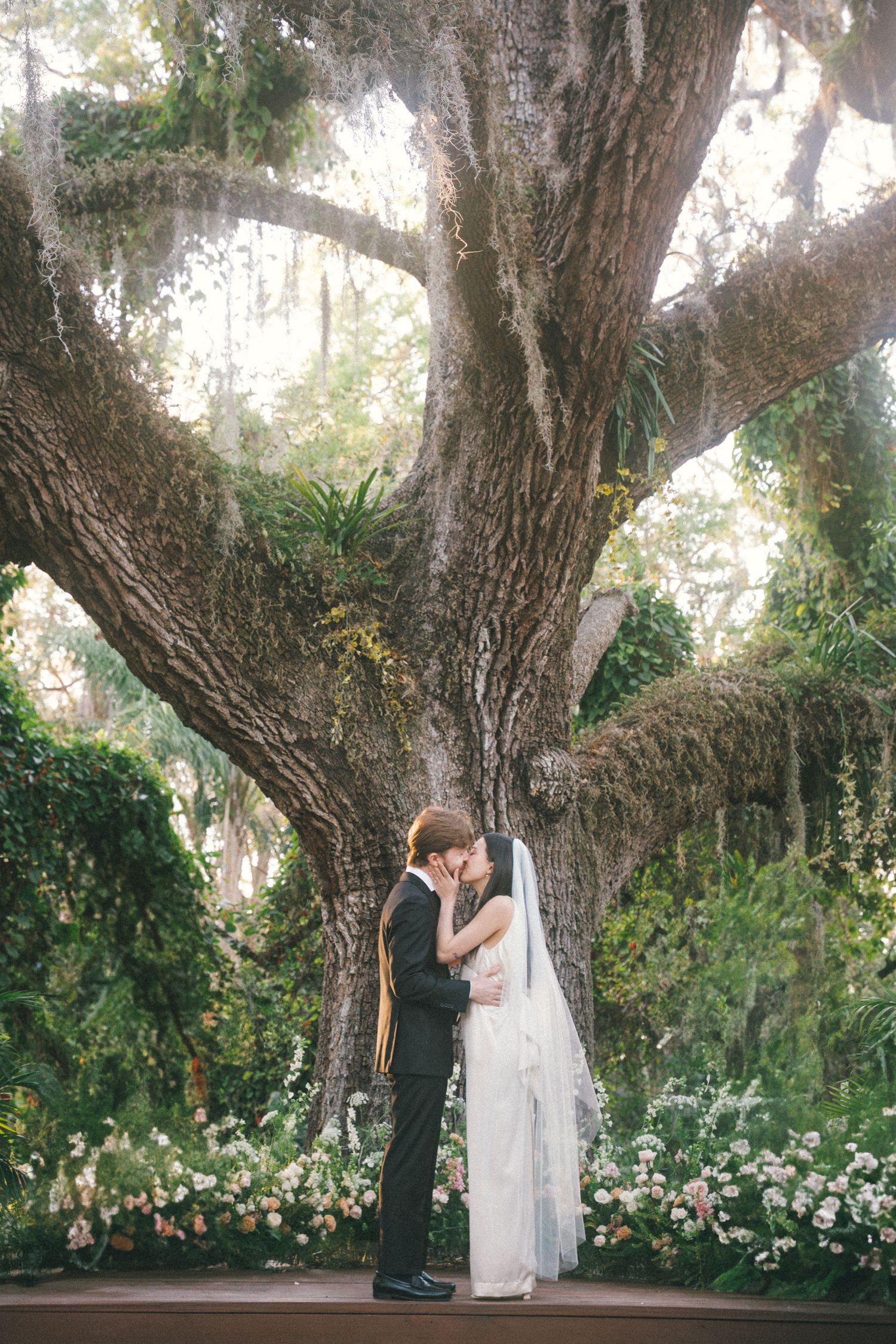Wedding ceremony photos under ancient oak trees with white floral arrangements.