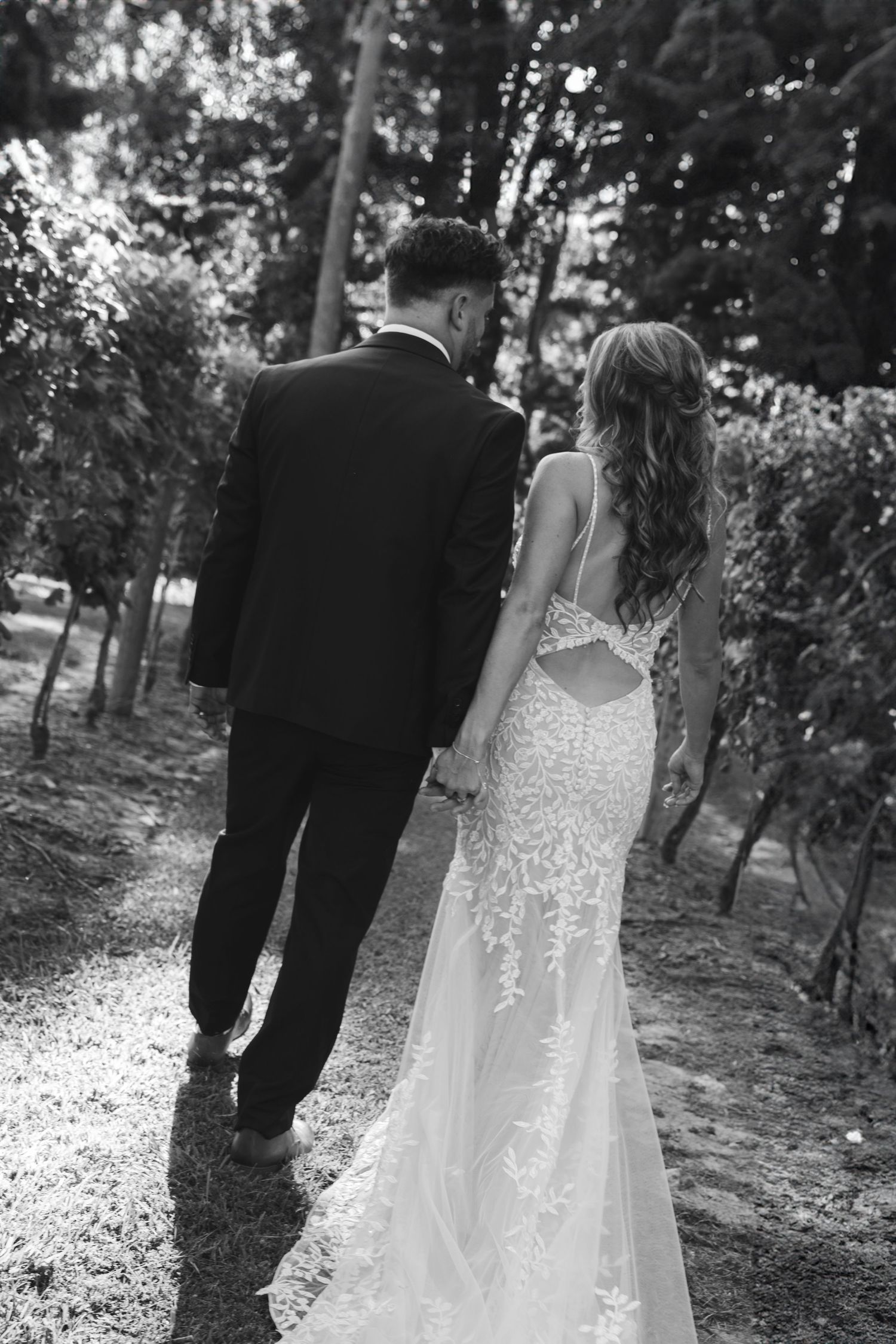 Black and white photo of a couple walking through a vineyard in wedding attire.