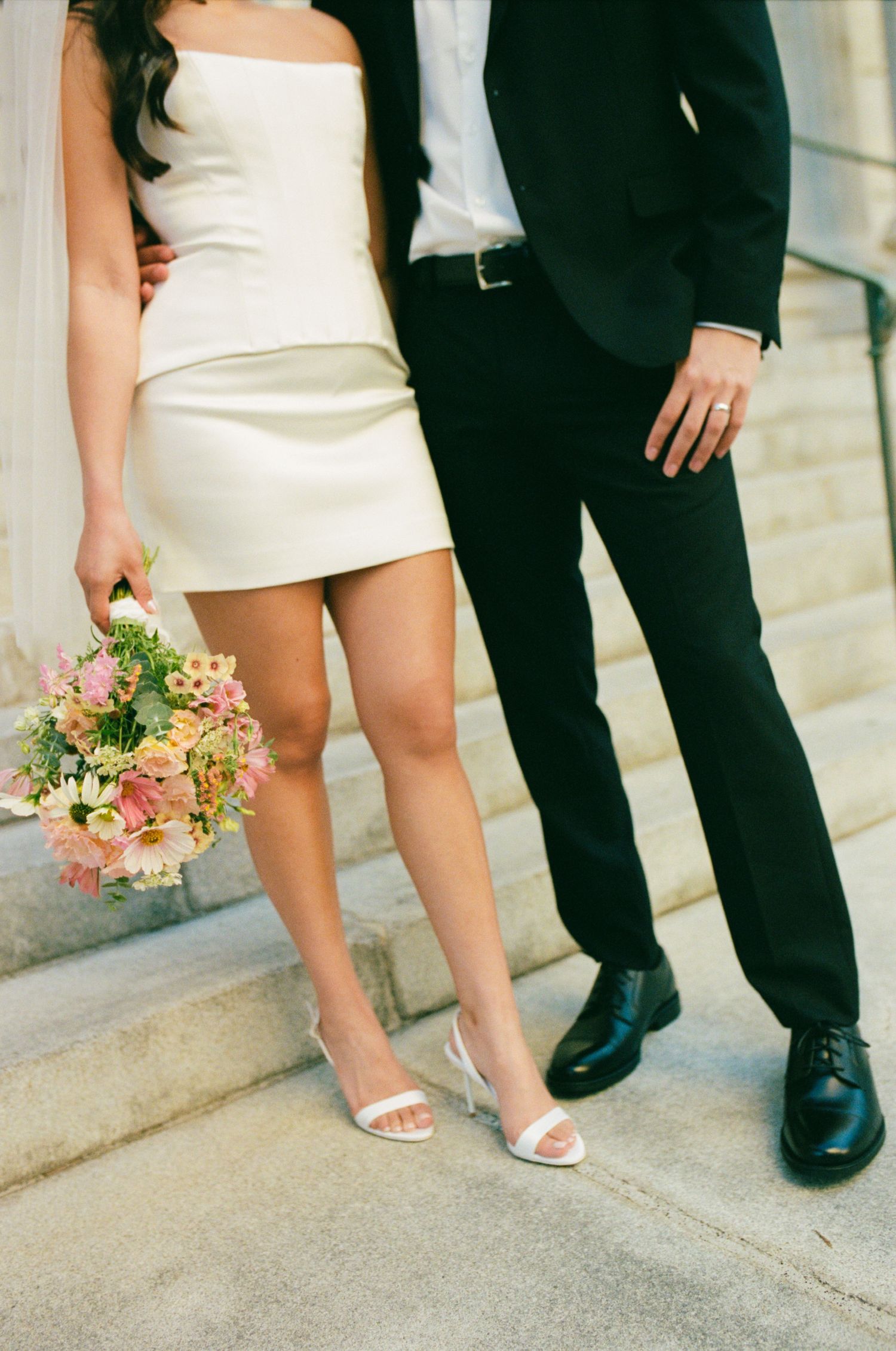 Close-up of bride and groom's feet and wedding attire on marble steps.