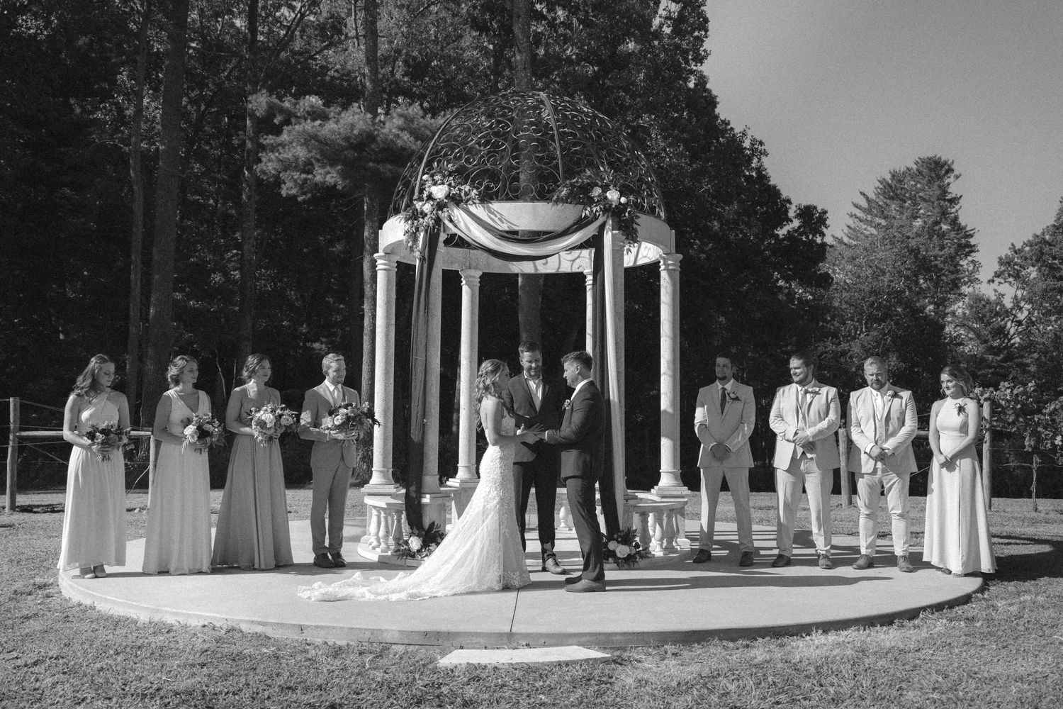 Wedding ceremony taking place under a draped gazebo with wedding party standing in formation.