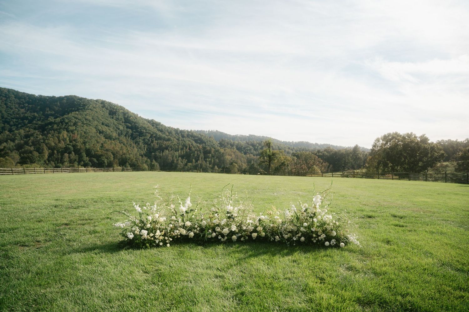 Floral arrangement on green meadow with mountain backdrop for outdoor wedding ceremony.