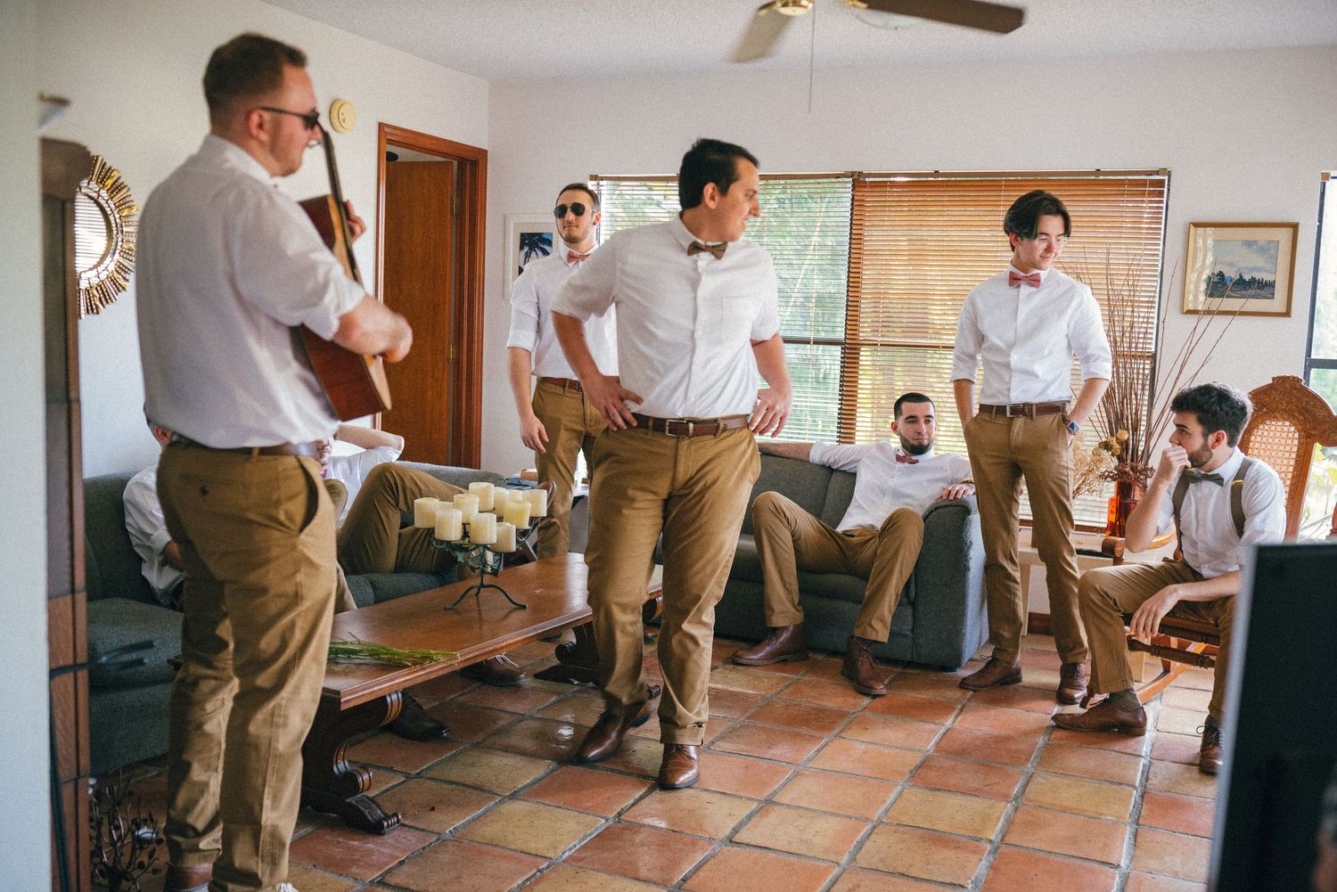 Group of groomsmen gathered in casual attire inside a rustic room with tile flooring.