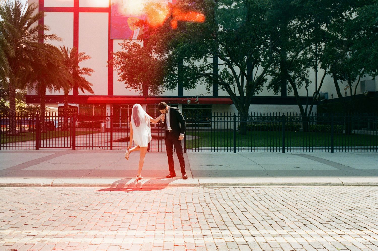 Silhouettes of couple walking against red-tinted sunset backdrop.