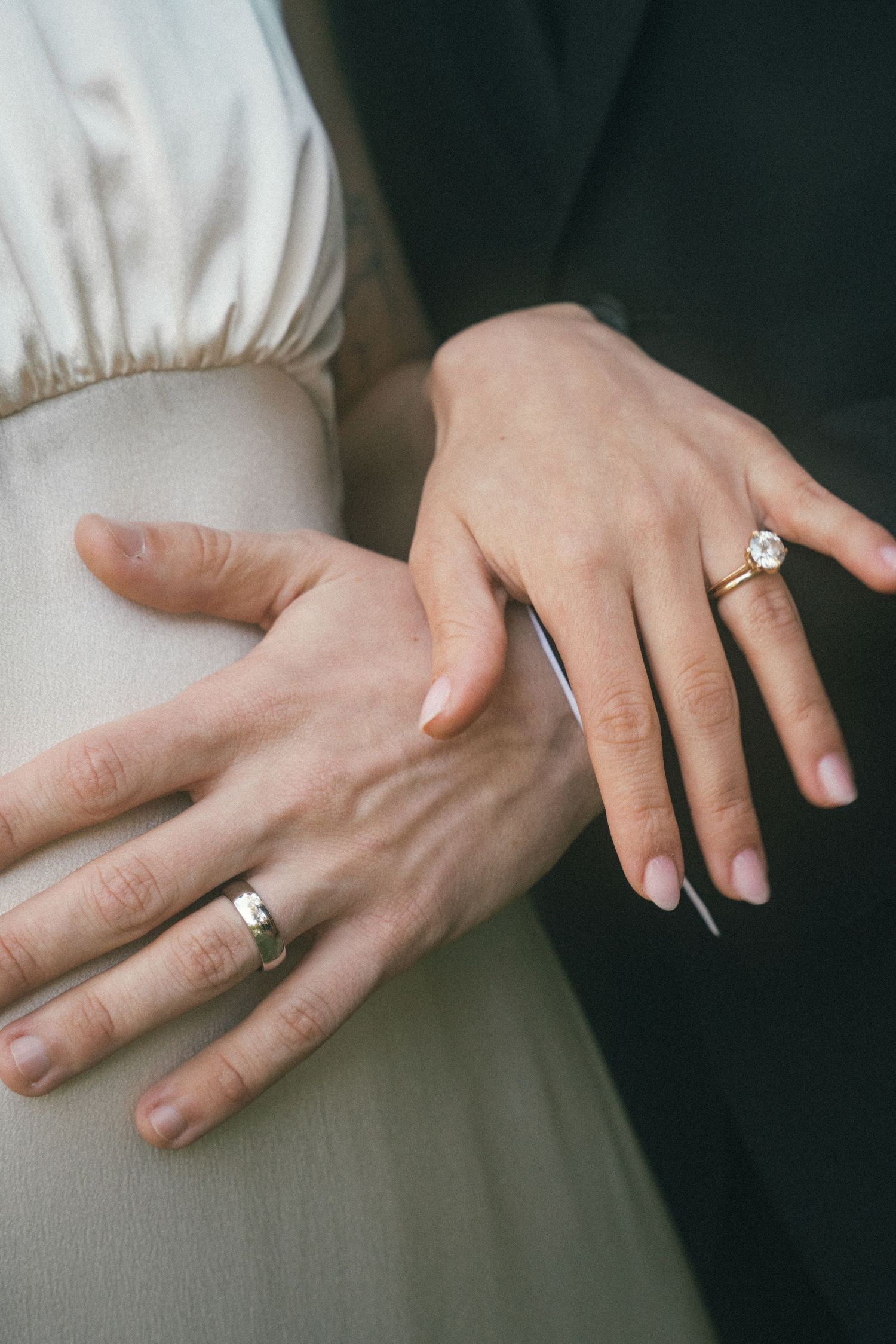 Close-up of two hands displaying wedding rings against a light colored dress.