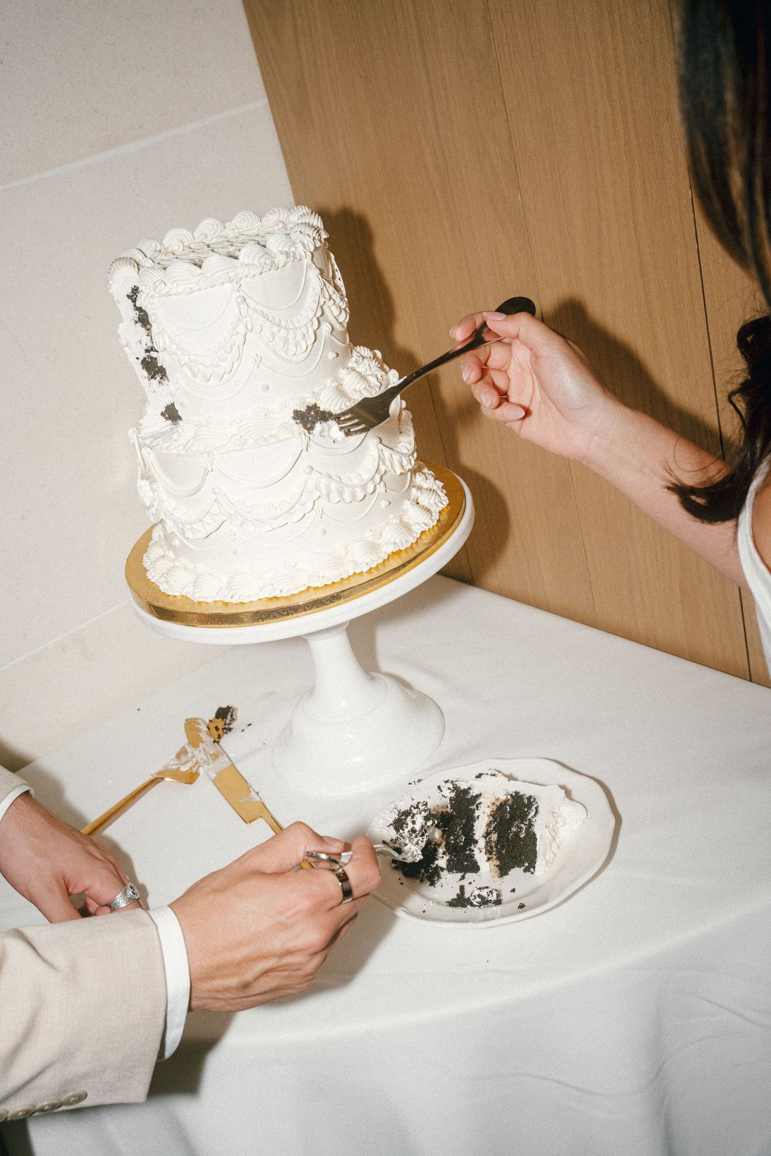 Wedding cake cutting sequence showing hands slicing into a white tiered cake with delicate frosting details.